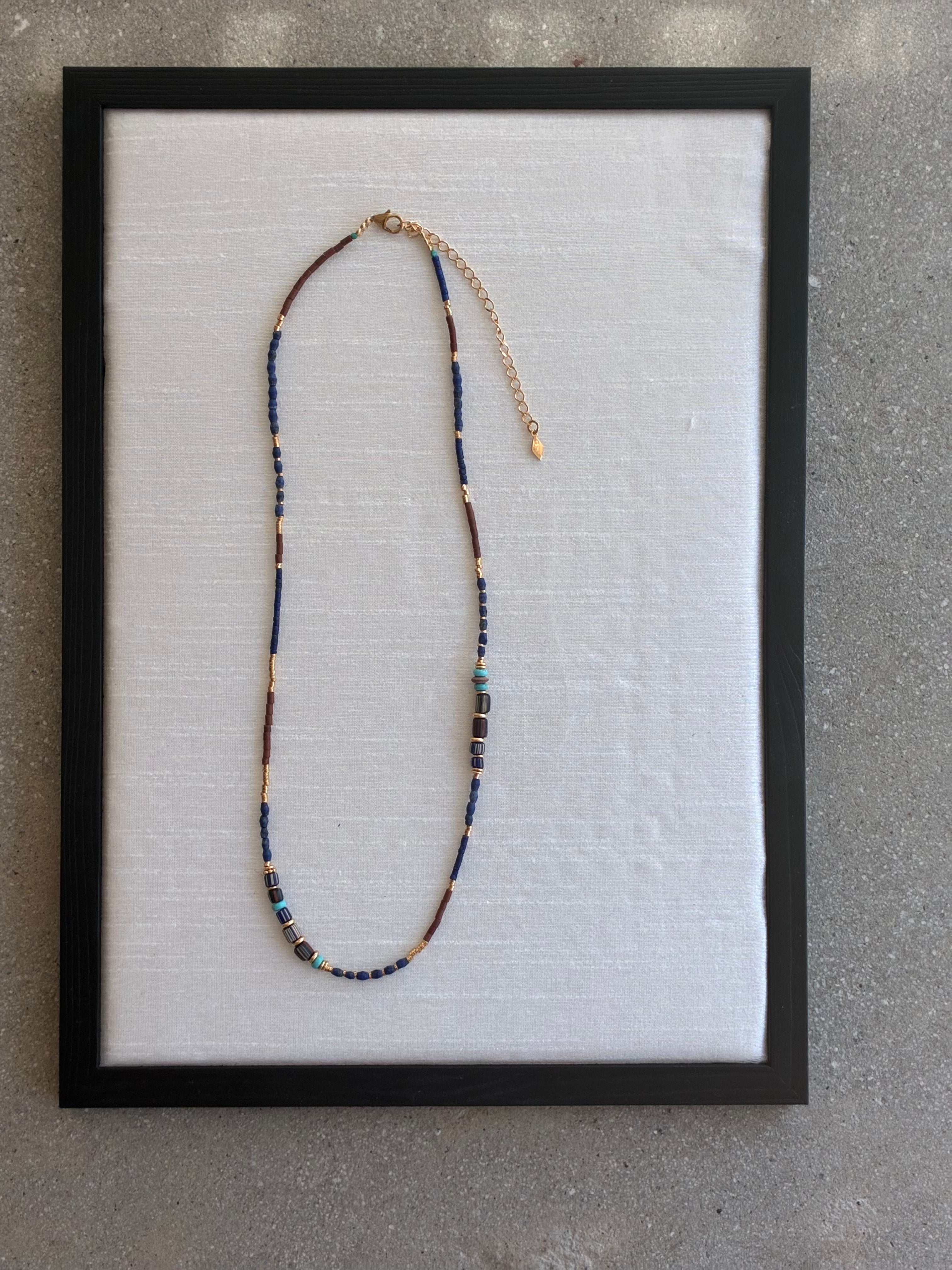 Gachon Pothier beaded necklace with blue and brown beads and 18kt gold plated hardware on a light gray background.