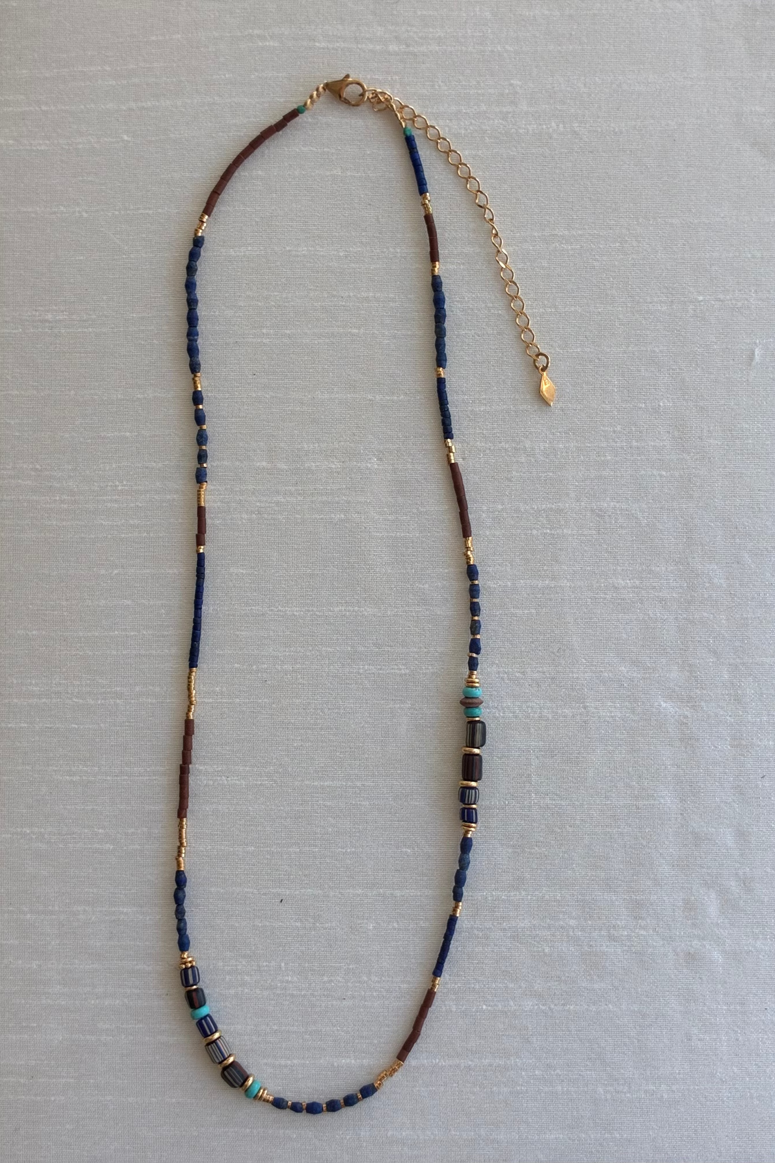 Gachon Pothier beaded necklace with blue and brown beads and 18kt gold plated hardware on a light gray background.