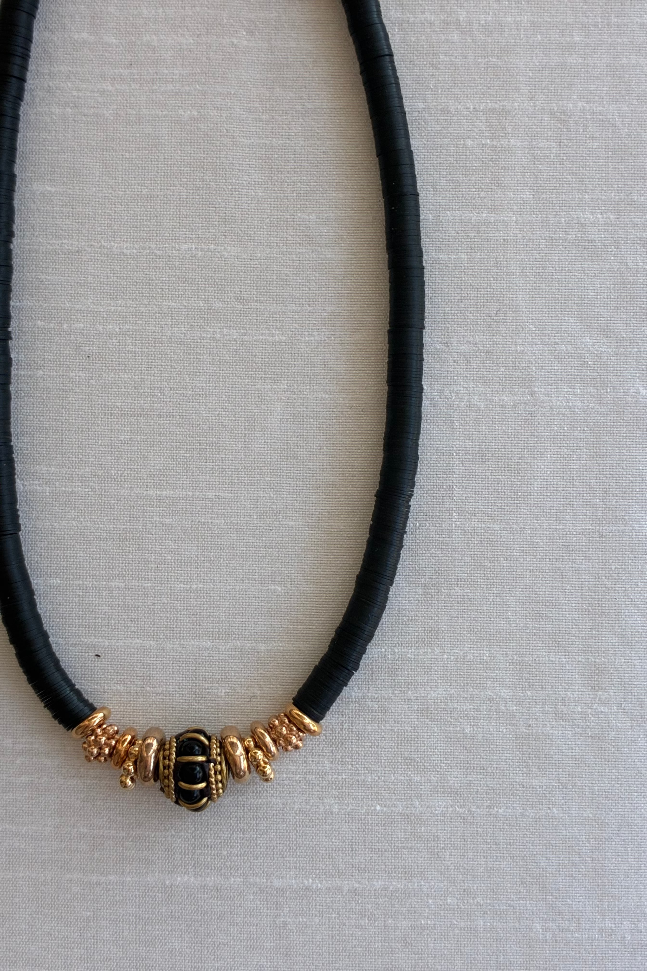 Close up of the Gachon Pothier Puka Bakelite beaded necklace with black beads and 18kt gold plated hardware on a light gray background.