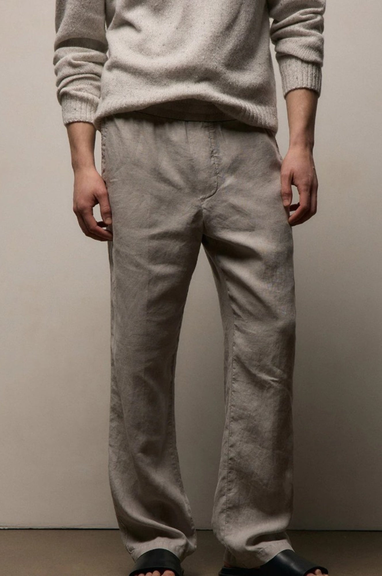 Person wearing a light gray sweater and pants against a plain background