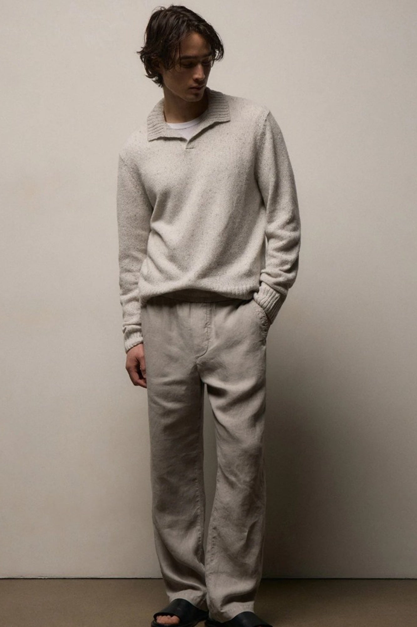 Man wearing a light gray sweater and pants against a plain background