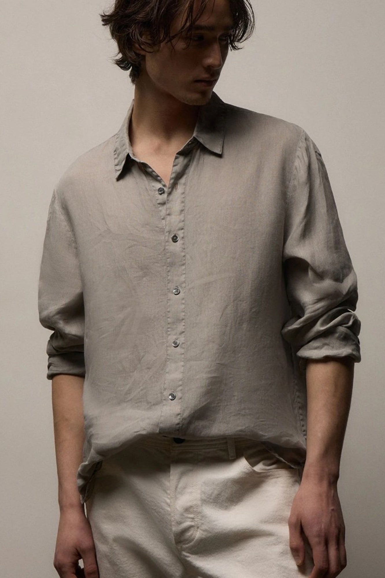 Person wearing a light gray button-up shirt and beige pants against a plain background