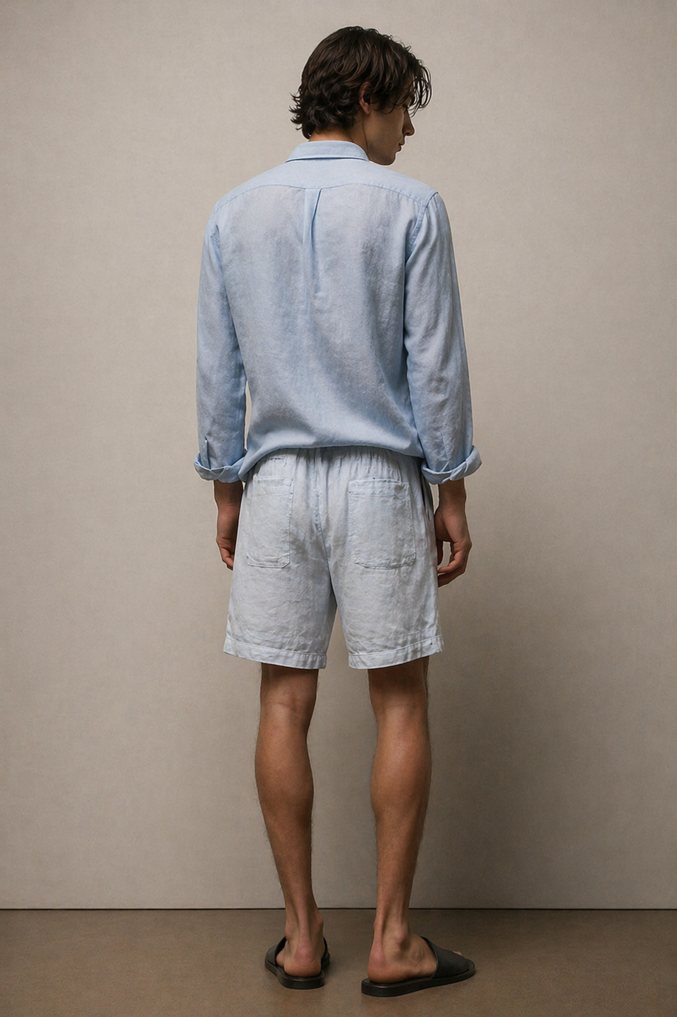 Man wearing a light blue shirt and white shorts against a beige wall.