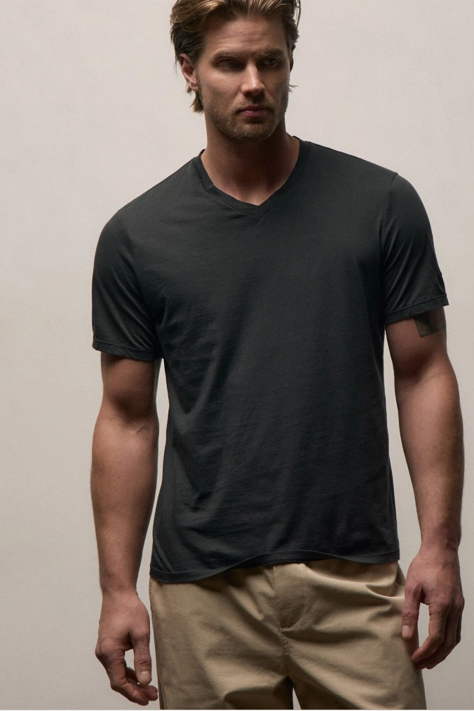 Man wearing a black t-shirt and beige pants against a plain background