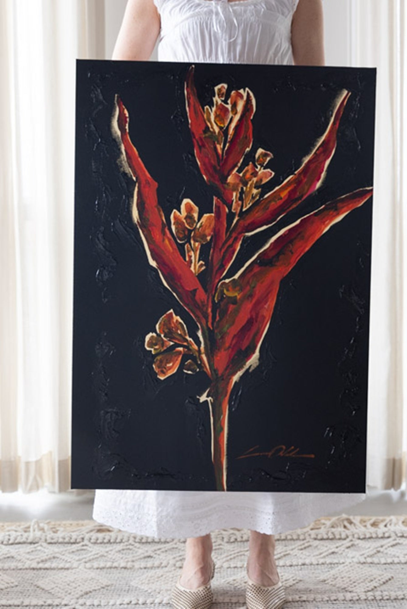 Person holding a painting of red flowers on a dark background