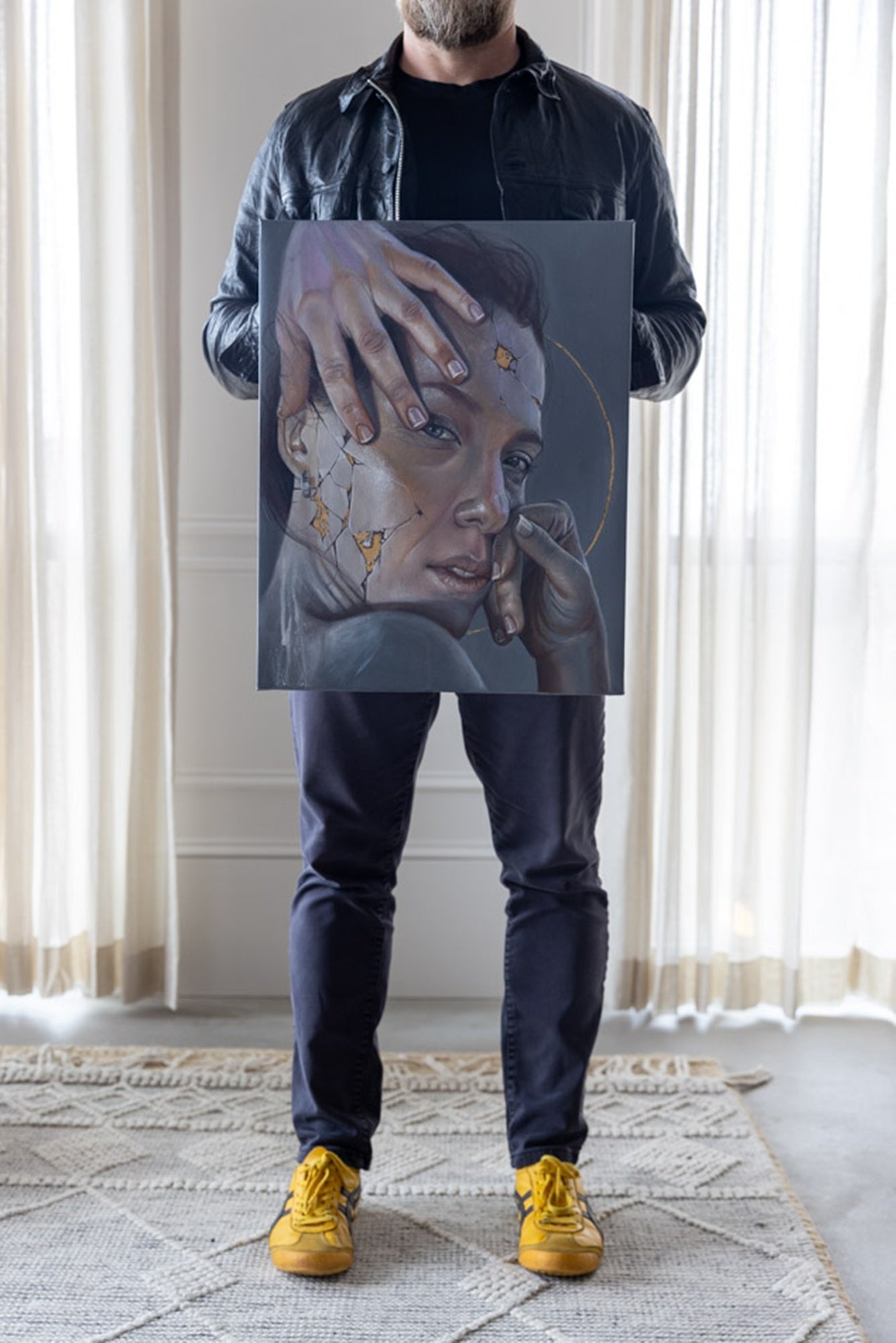 Person holding a painting of a woman with stars on her face in a room with light-colored curtains.