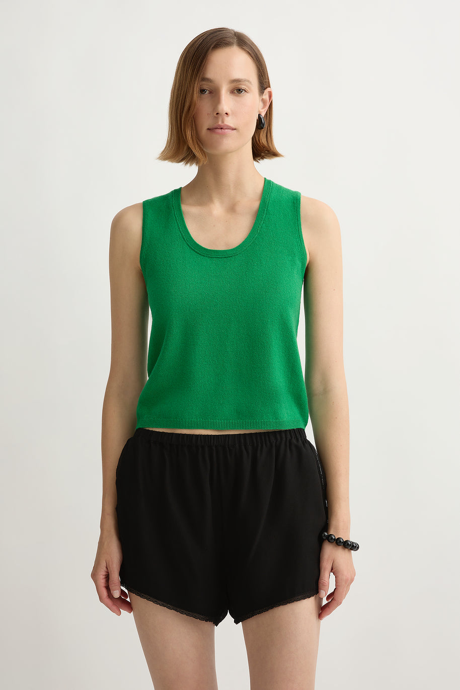 Woman wearing Posse Freddie Sweater Tank in green standing in front of a white background.
