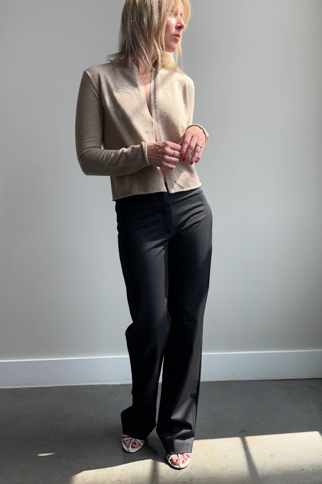 Woman wearing a beige cardigan and black pants against a plain background