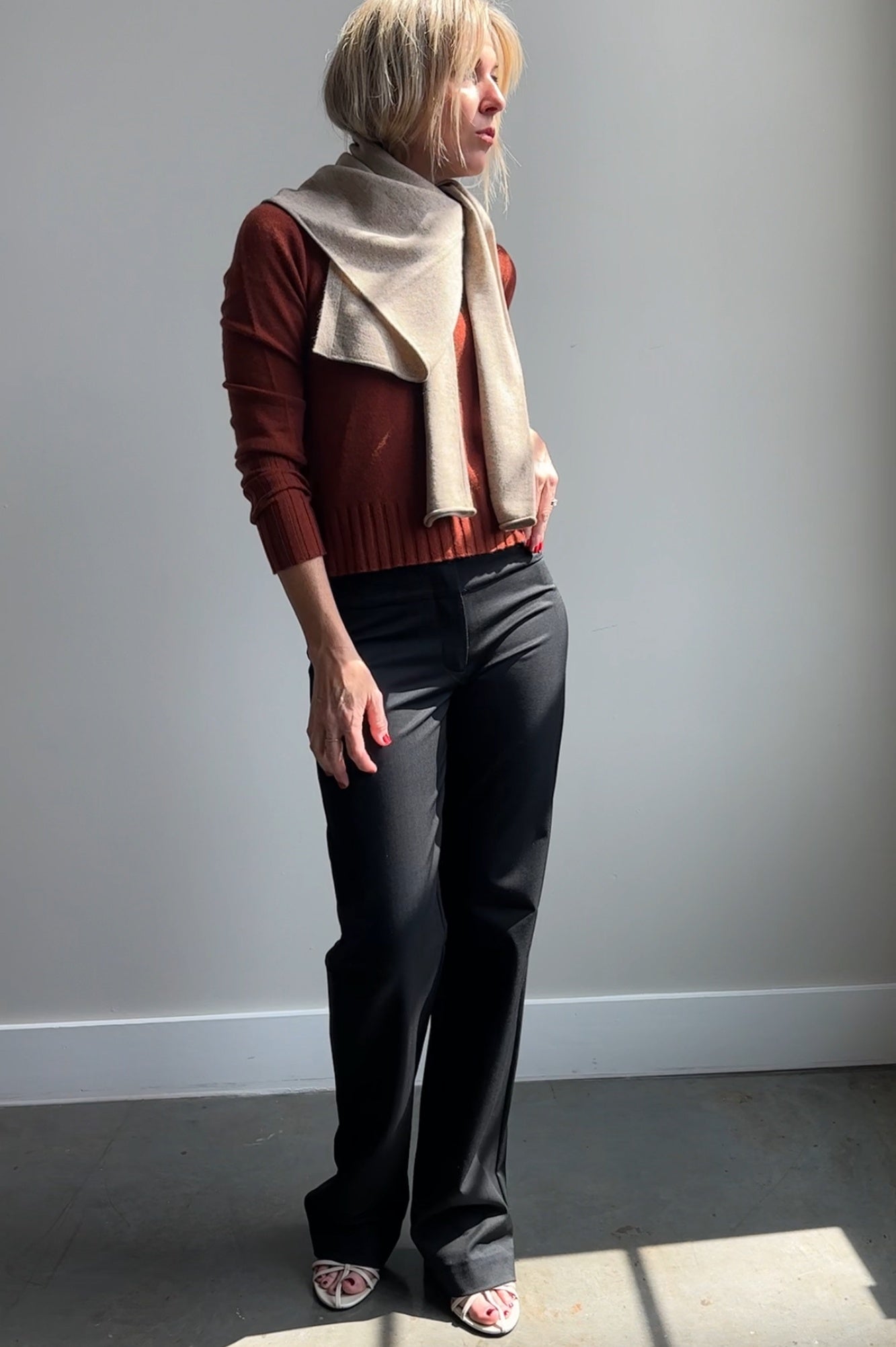 Person wearing a red sweater, black pants, and a beige scarf against a plain background