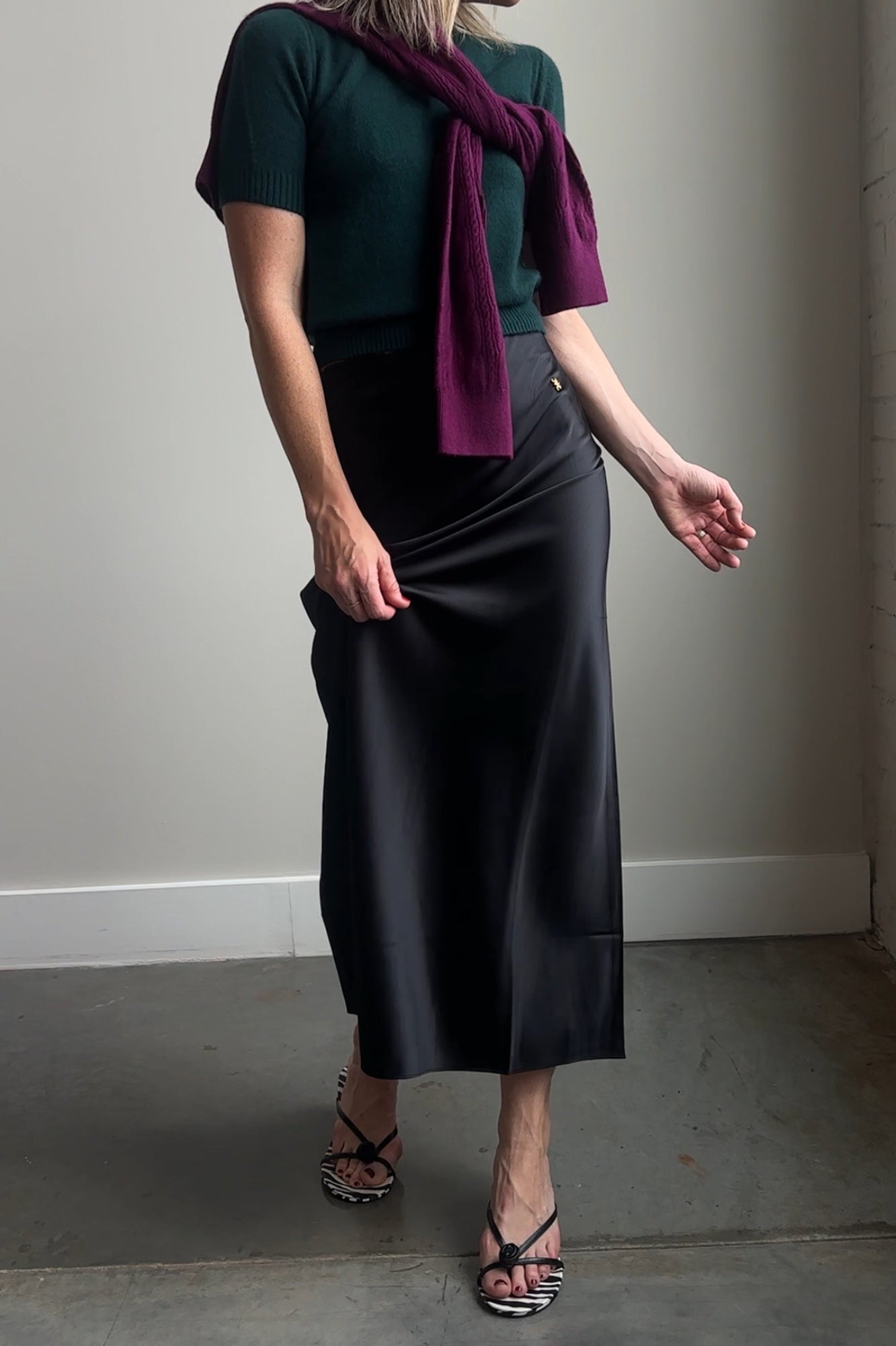 Person wearing a green top, black skirt, and purple scarf against a plain wall.