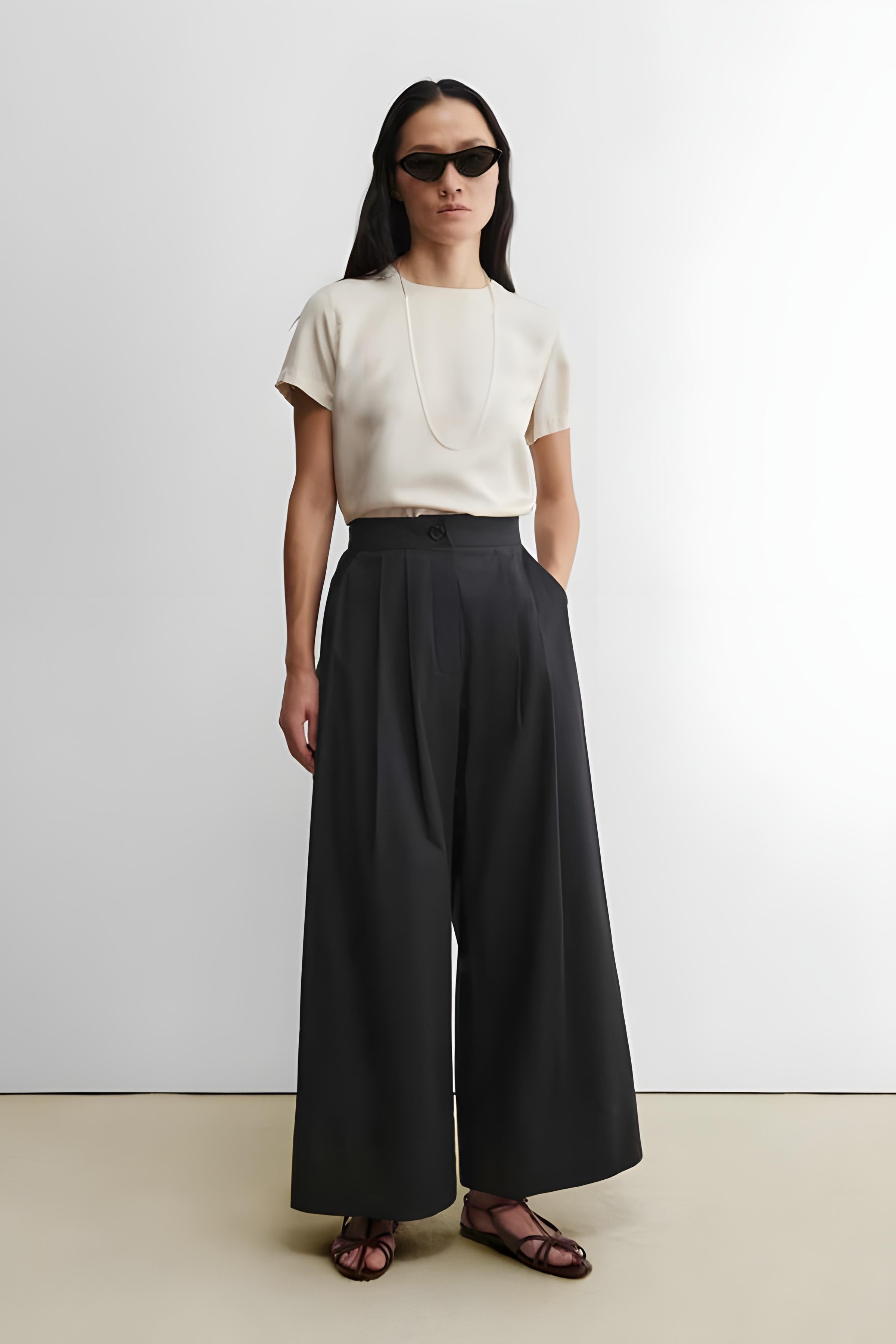 Woman wearing a white top and black wide-leg pants against a white background