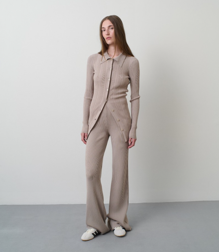 Woman wearing a beige knit suit standing against a plain background