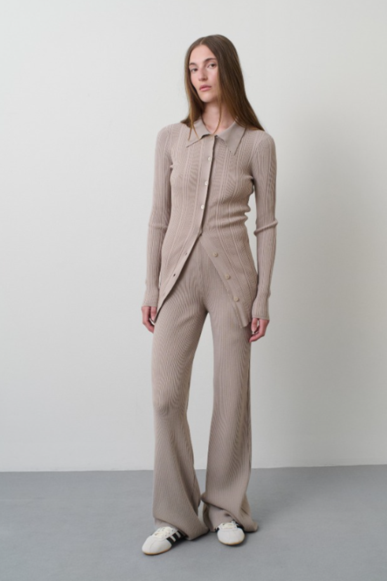 Woman wearing a beige knit suit standing against a plain background