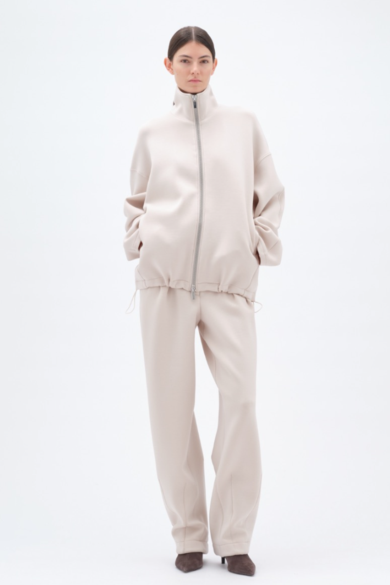Woman wearing a beige soft jacket and matching pants on a white background