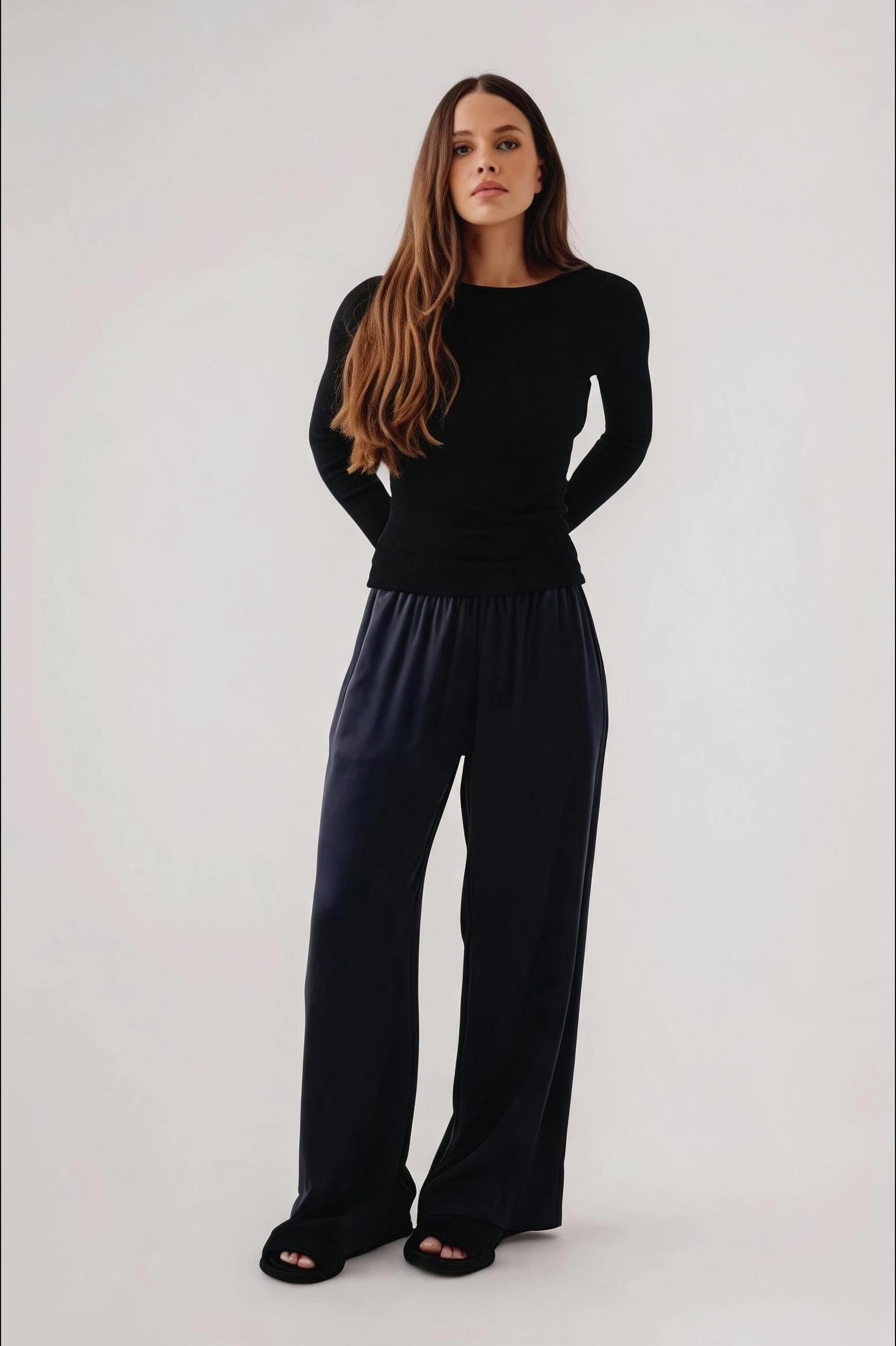 A woman modeling a black long-sleeve top and dark navy wide-leg pants against a plain light gray studio background.