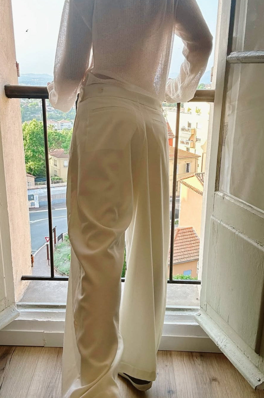 Person wearing a white outfit standing in a room with an open door and view of buildings outside.