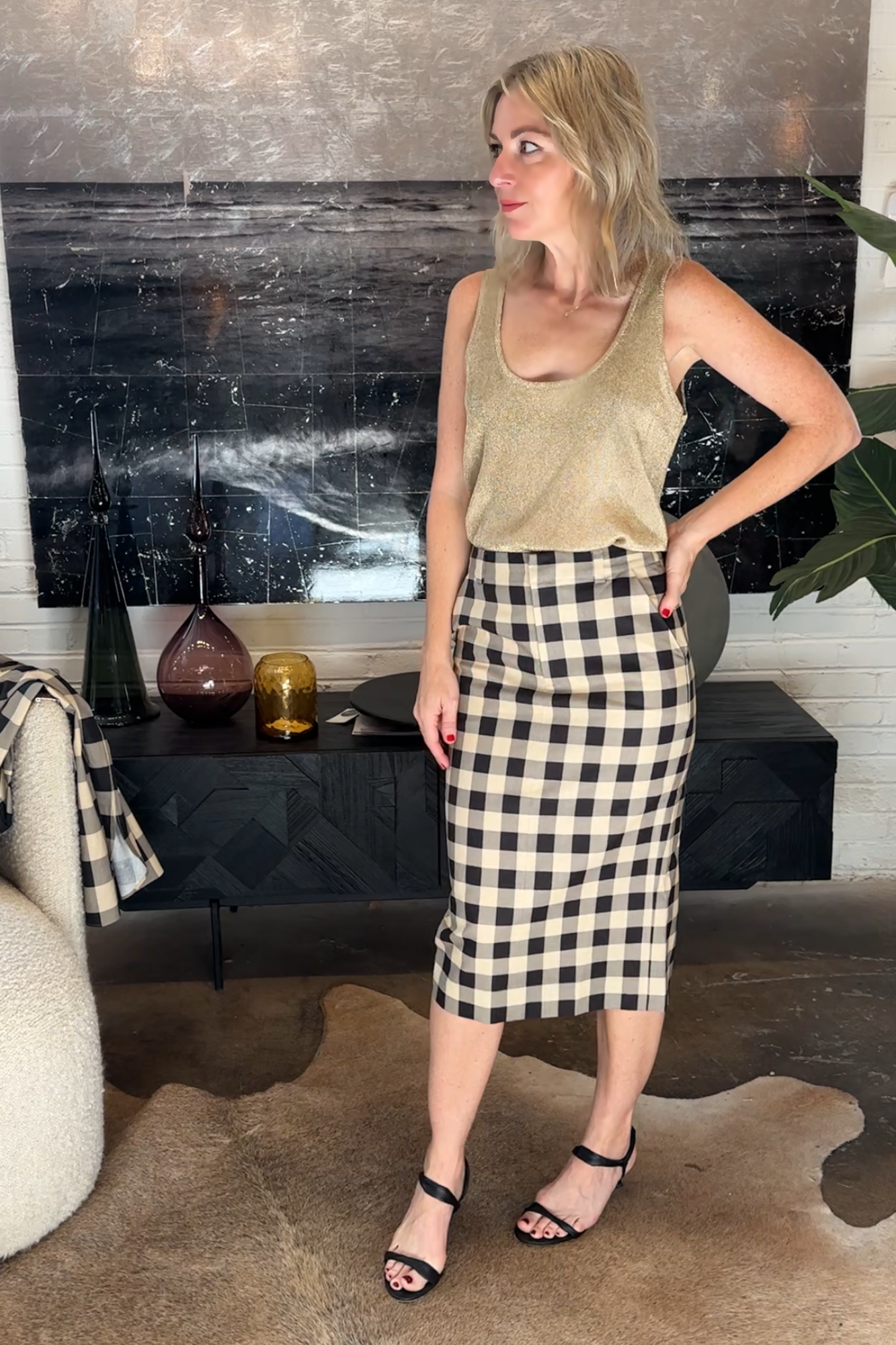 Woman in a checkered skirt and tank top standing in a room with decorative elements.