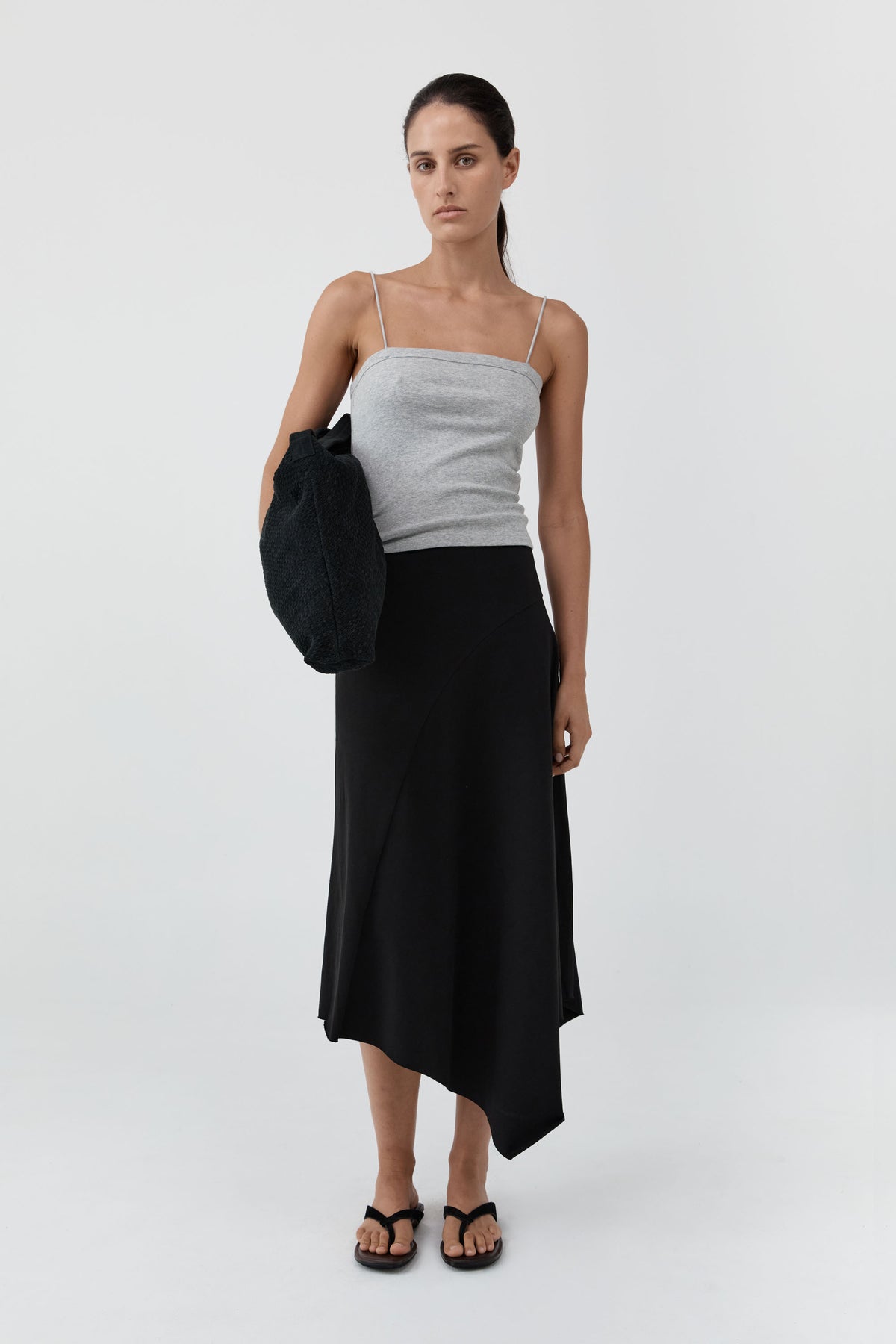 Woman wearing a white top and black skirt holding a black bag on a white background