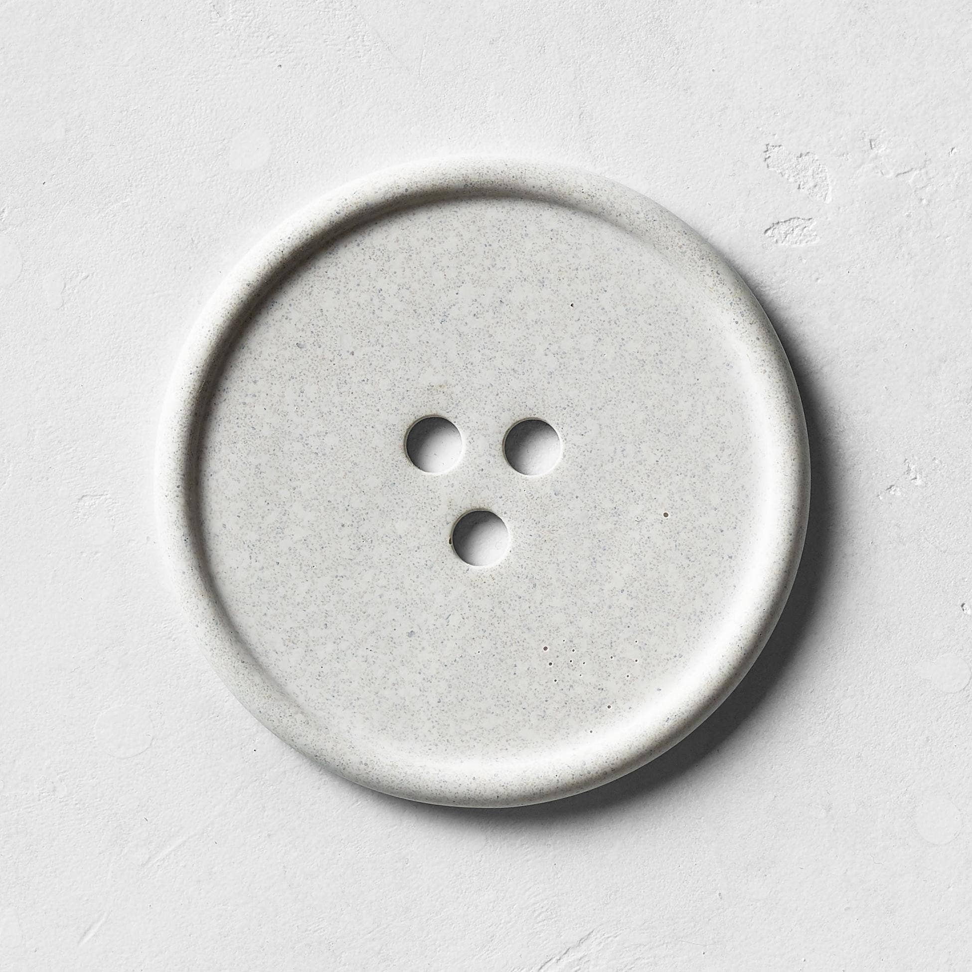 Round ceramic button with three holes on a light gray background