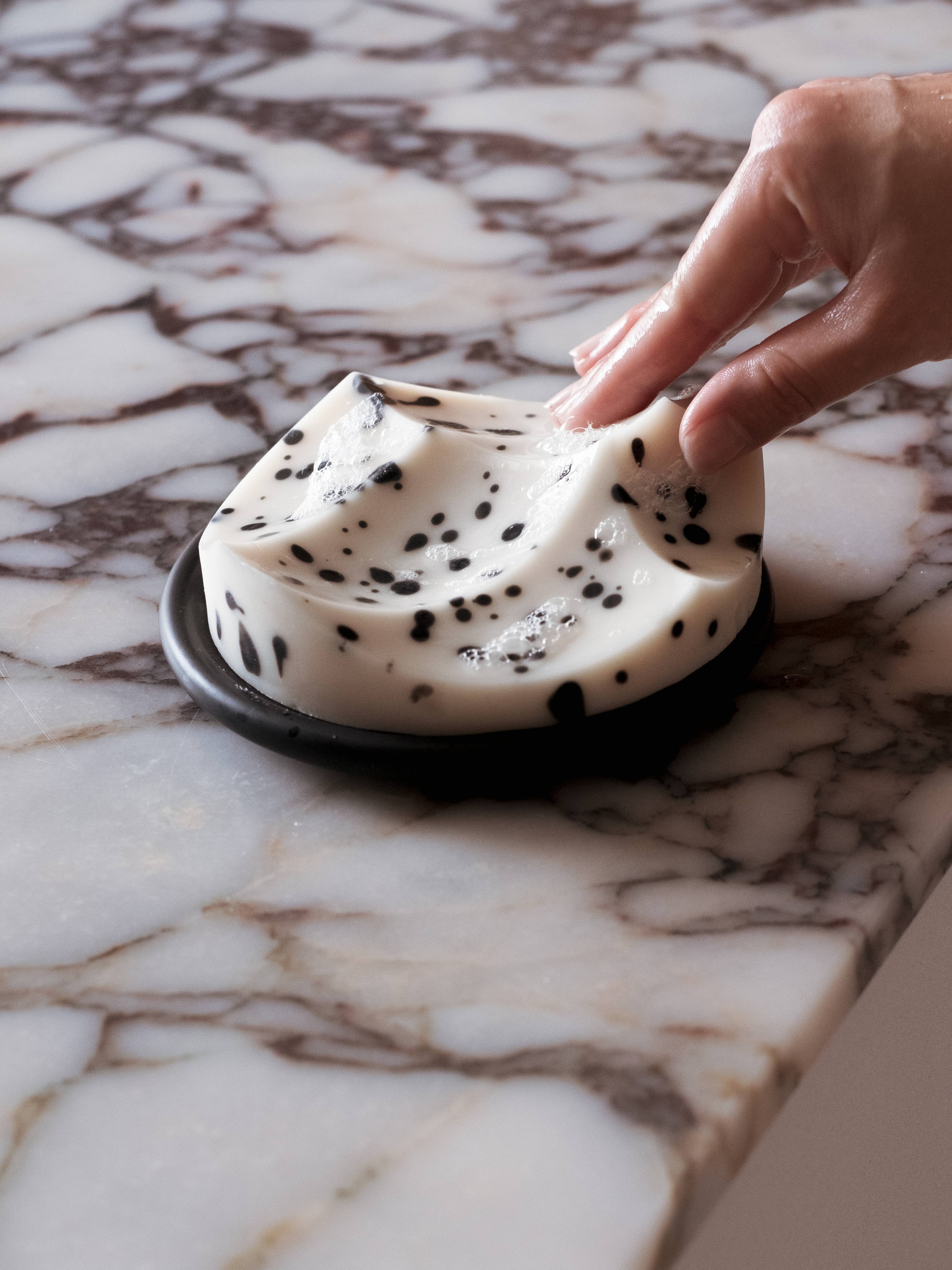 Hand touching a creamy dessert with chocolate chips on a marble surface