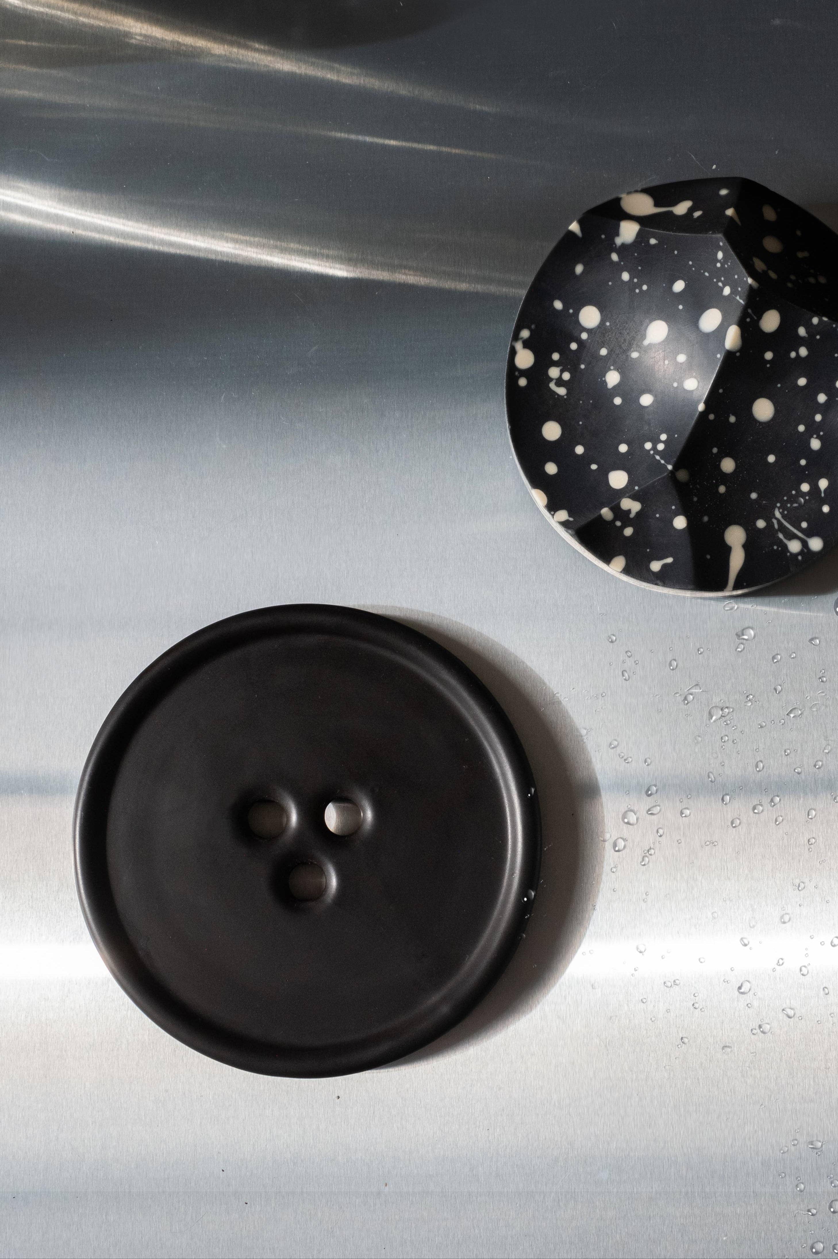 Two buttons, one black and one with a speckled pattern, on a metallic surface.