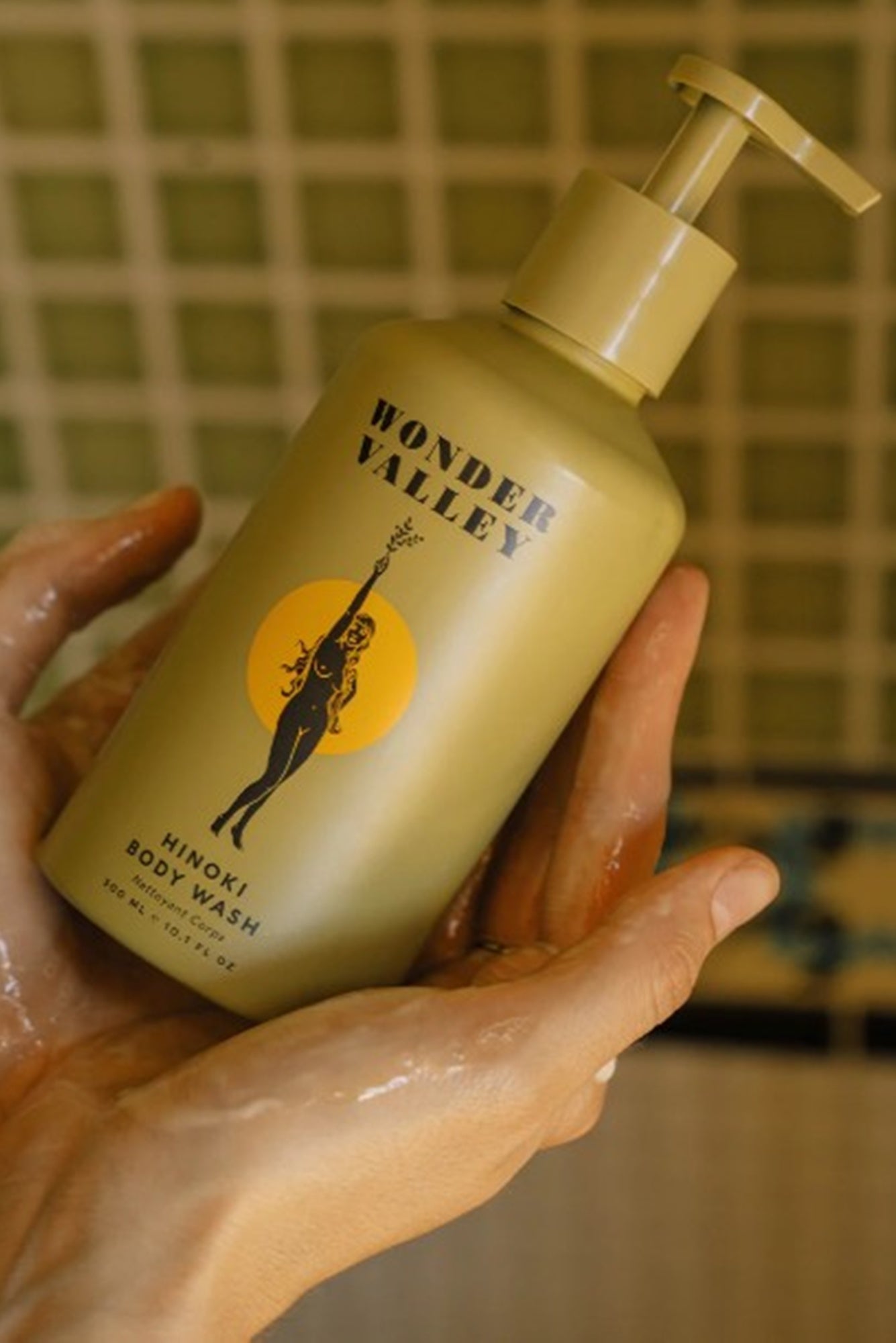 Hand holding a bottle of Wonder Valley body wash with a tiled background