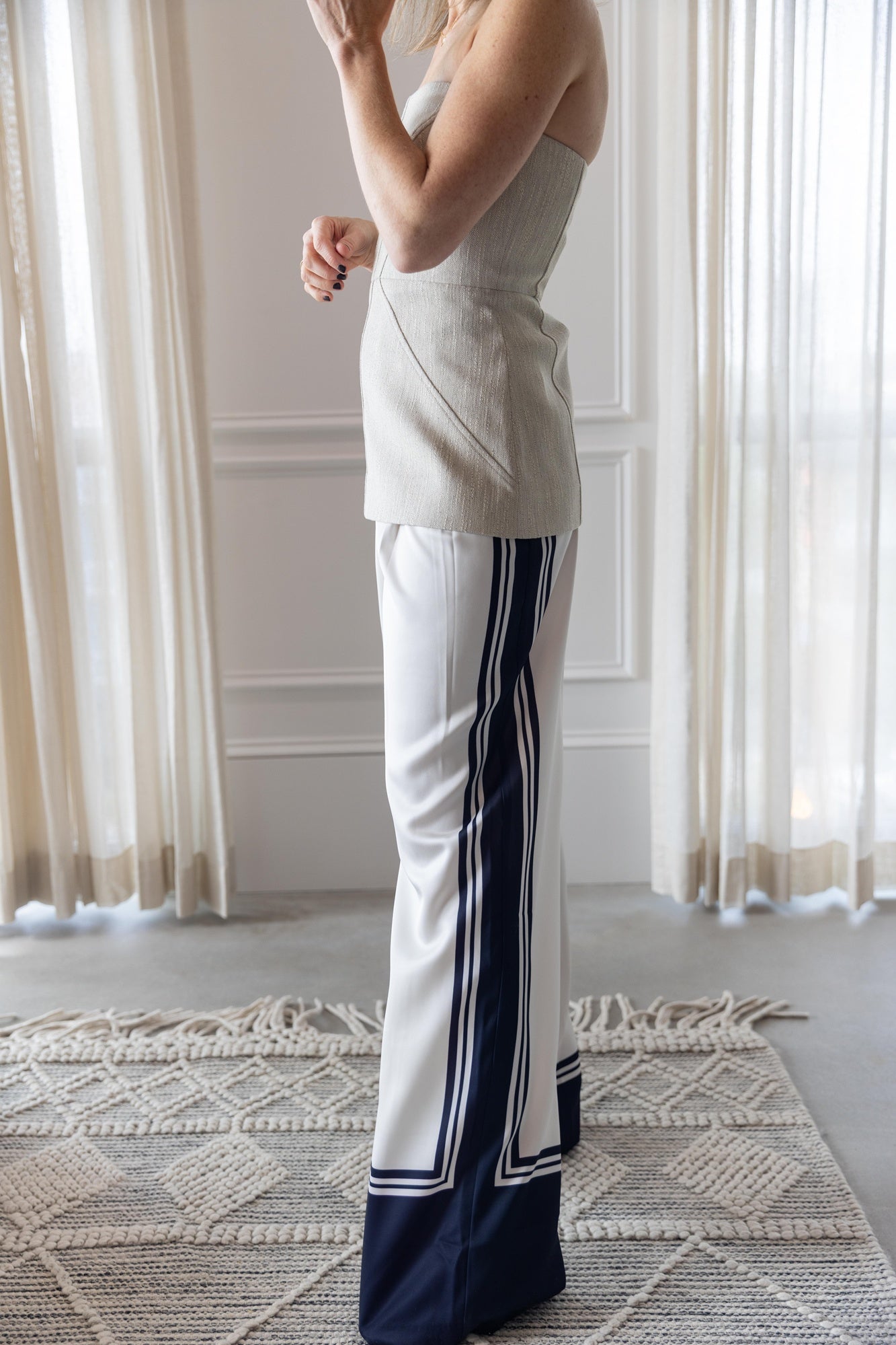 Woman wearing a-emery lovett top and seroya marlowe satin pants standing in a room with tasseled rug and white curtains.