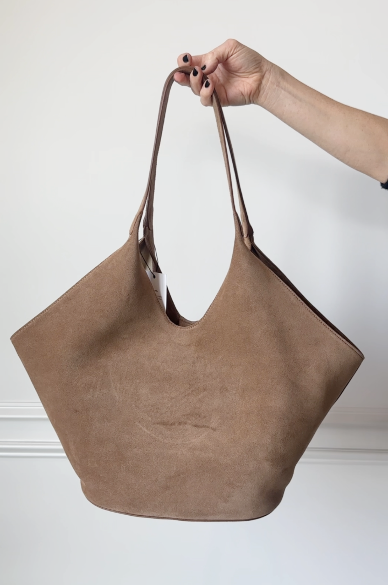 Brown suede handbag held by a hand against a white background