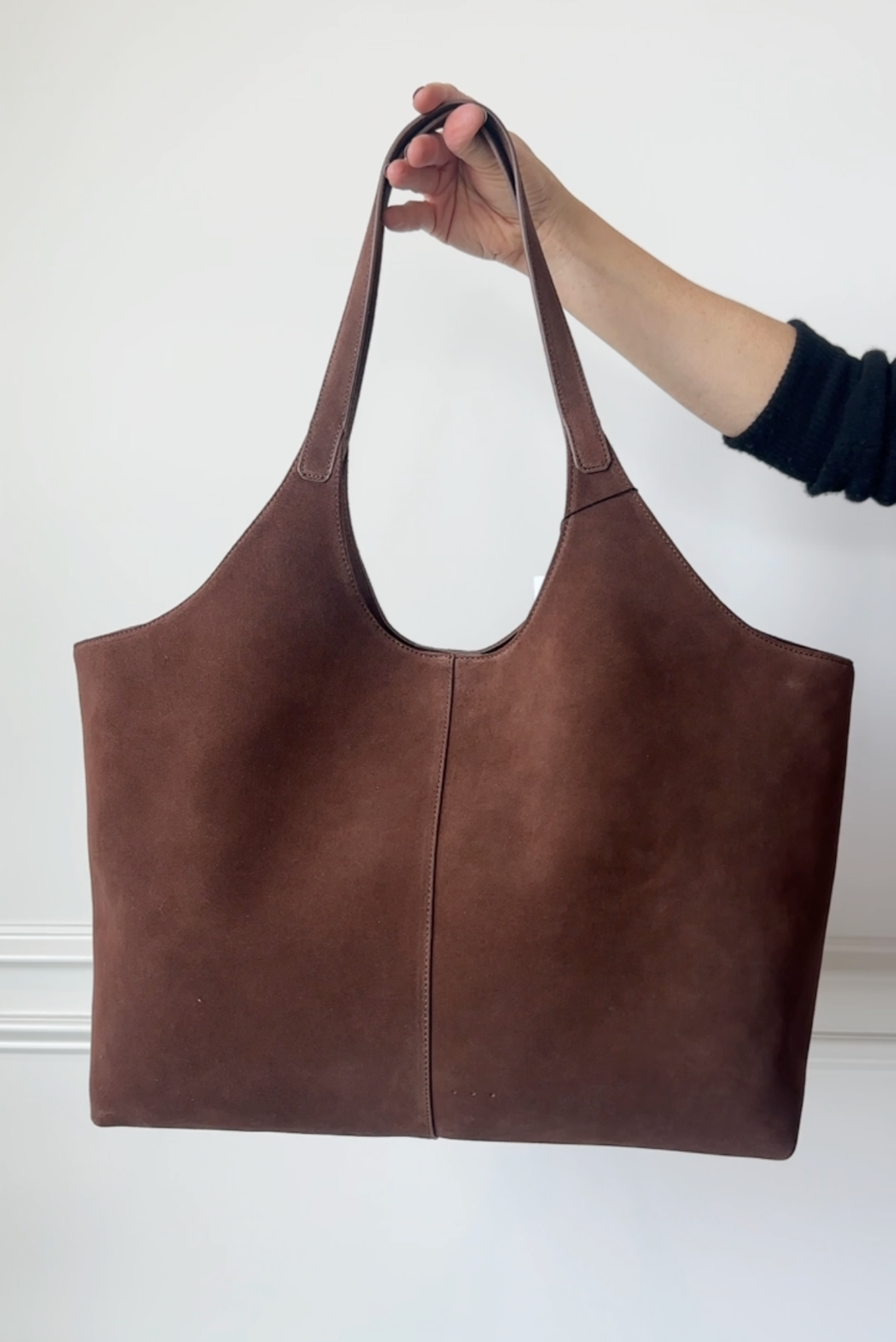 Brown leather tote bag held by a hand against a white background