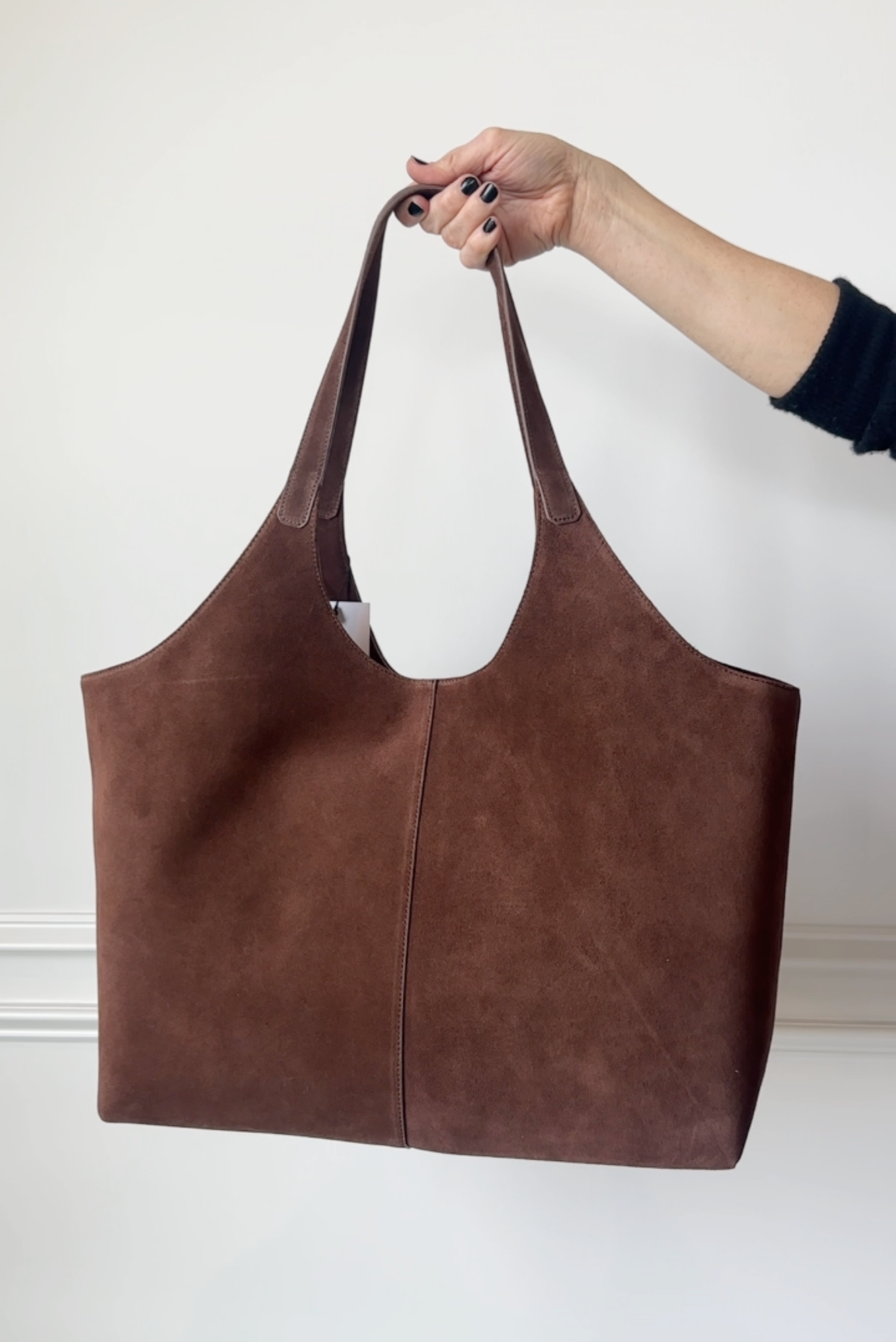 Brown leather tote bag held by a hand against a white background