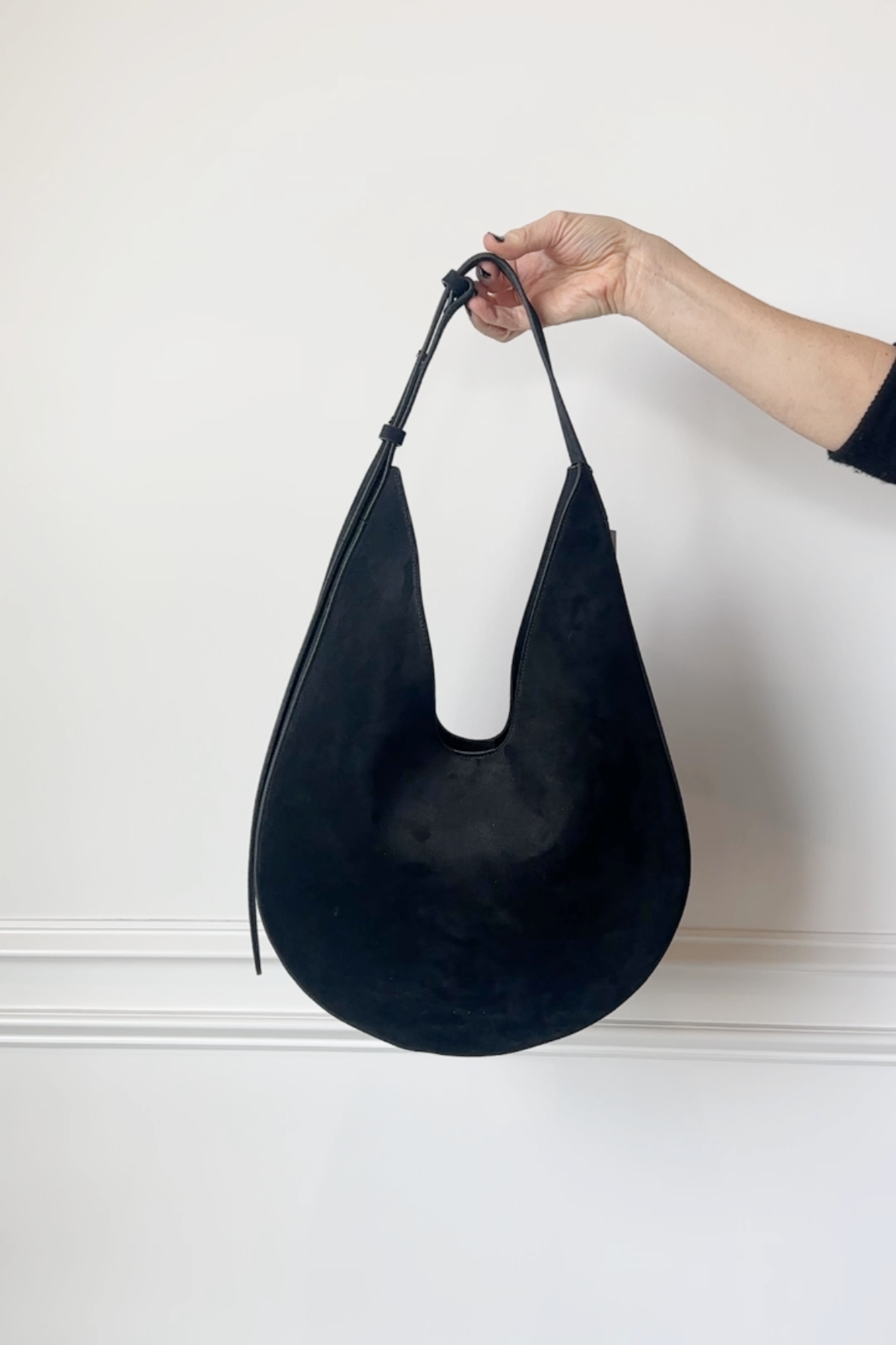 Black handbag held by a hand against a white background