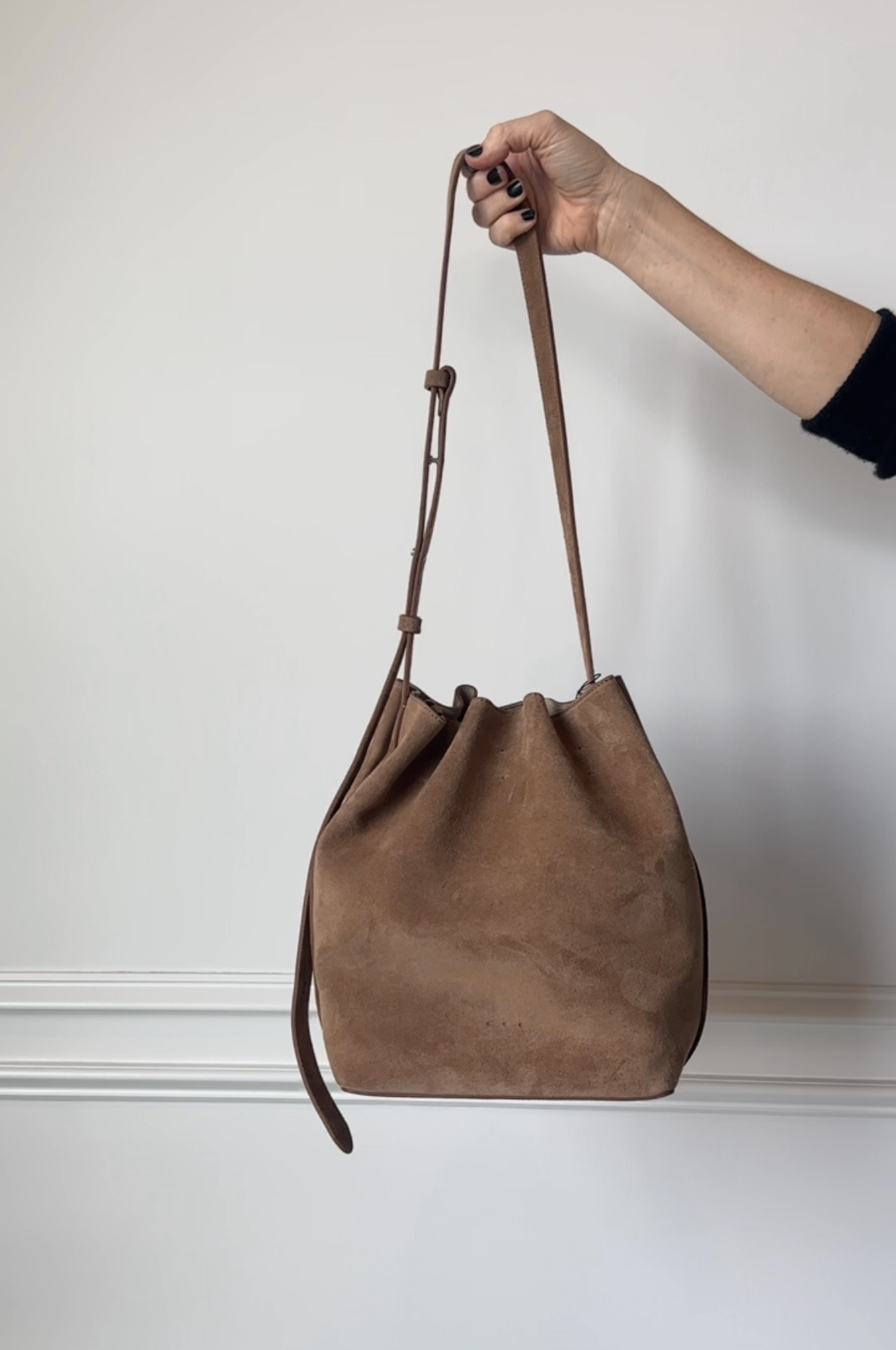 Brown leather bag held by a hand against a plain background