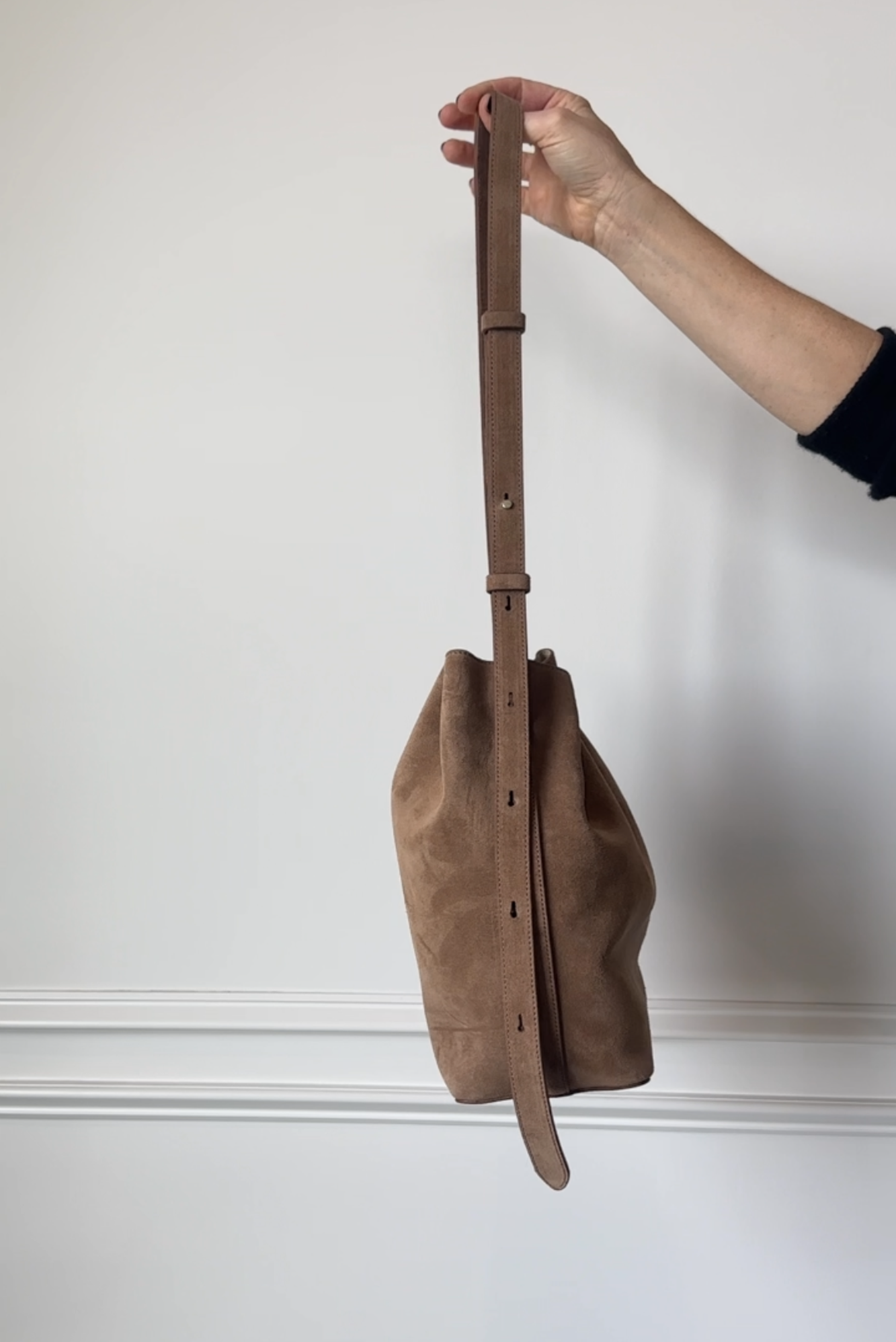 Brown leather bag held by a hand against a white wall