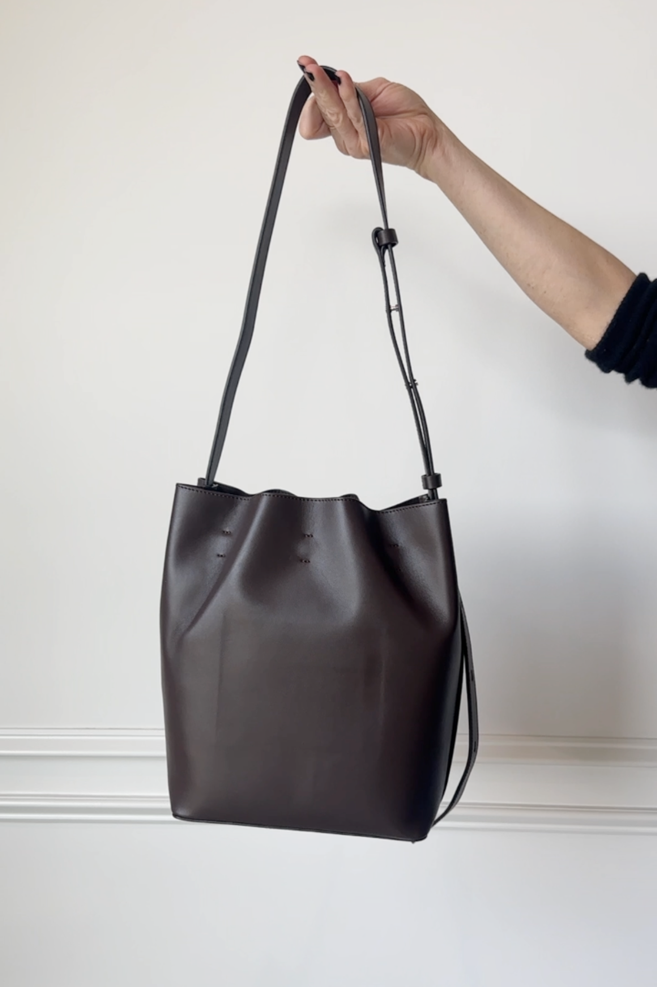 Black leather handbag held by a person against a white background