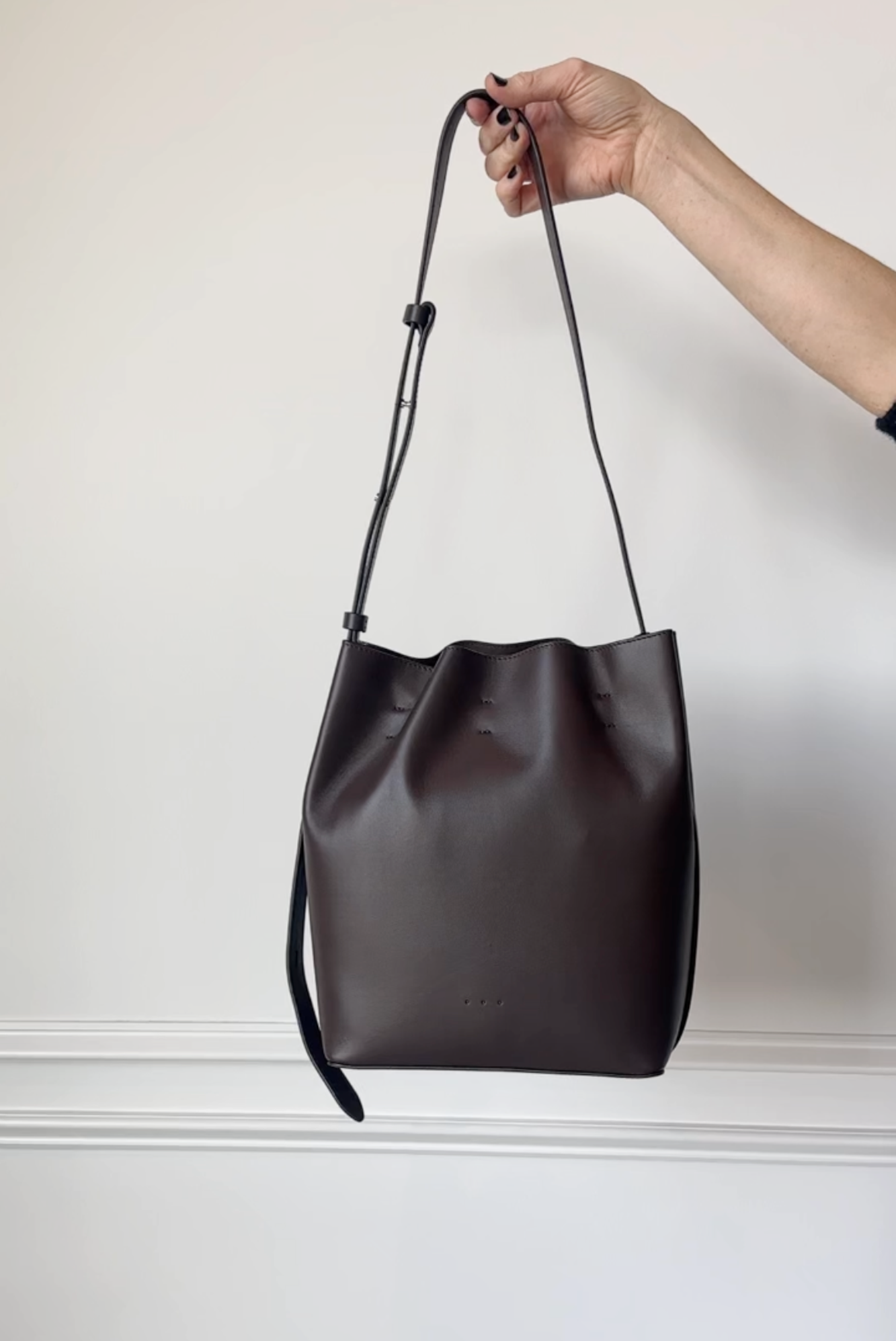 Black leather handbag held by a hand against a light background