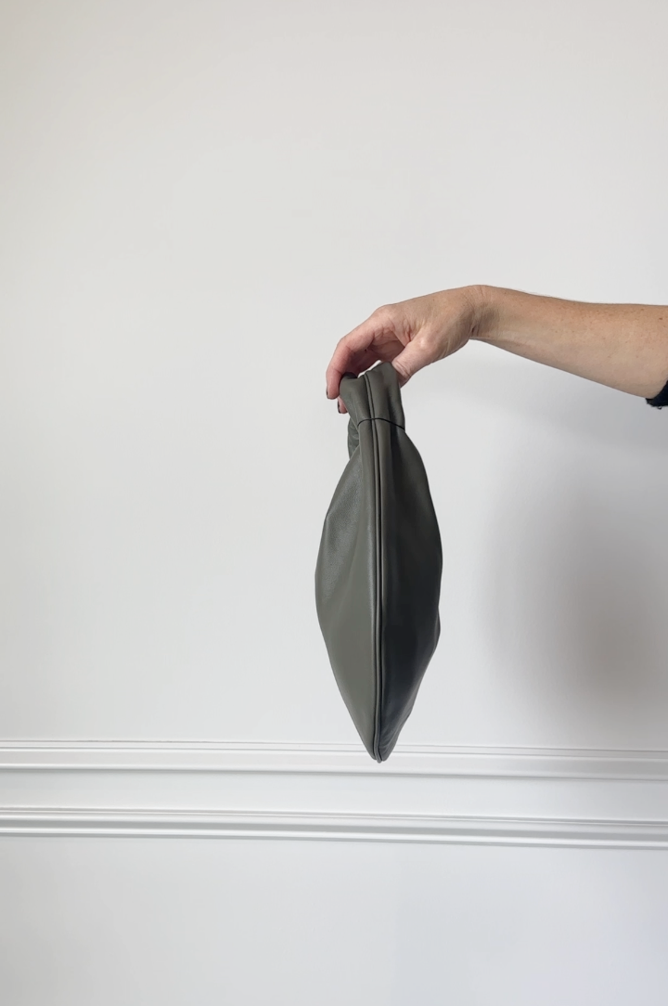 Person holding a dark gray clutch against a white background