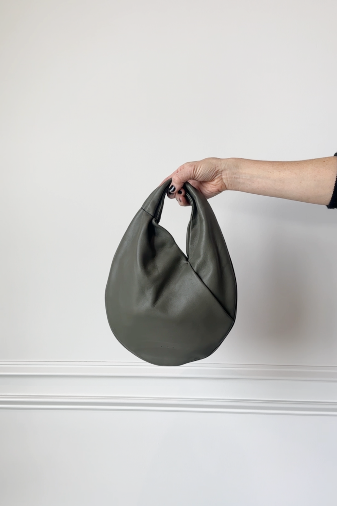 Hand holding a green handbag against a white background
