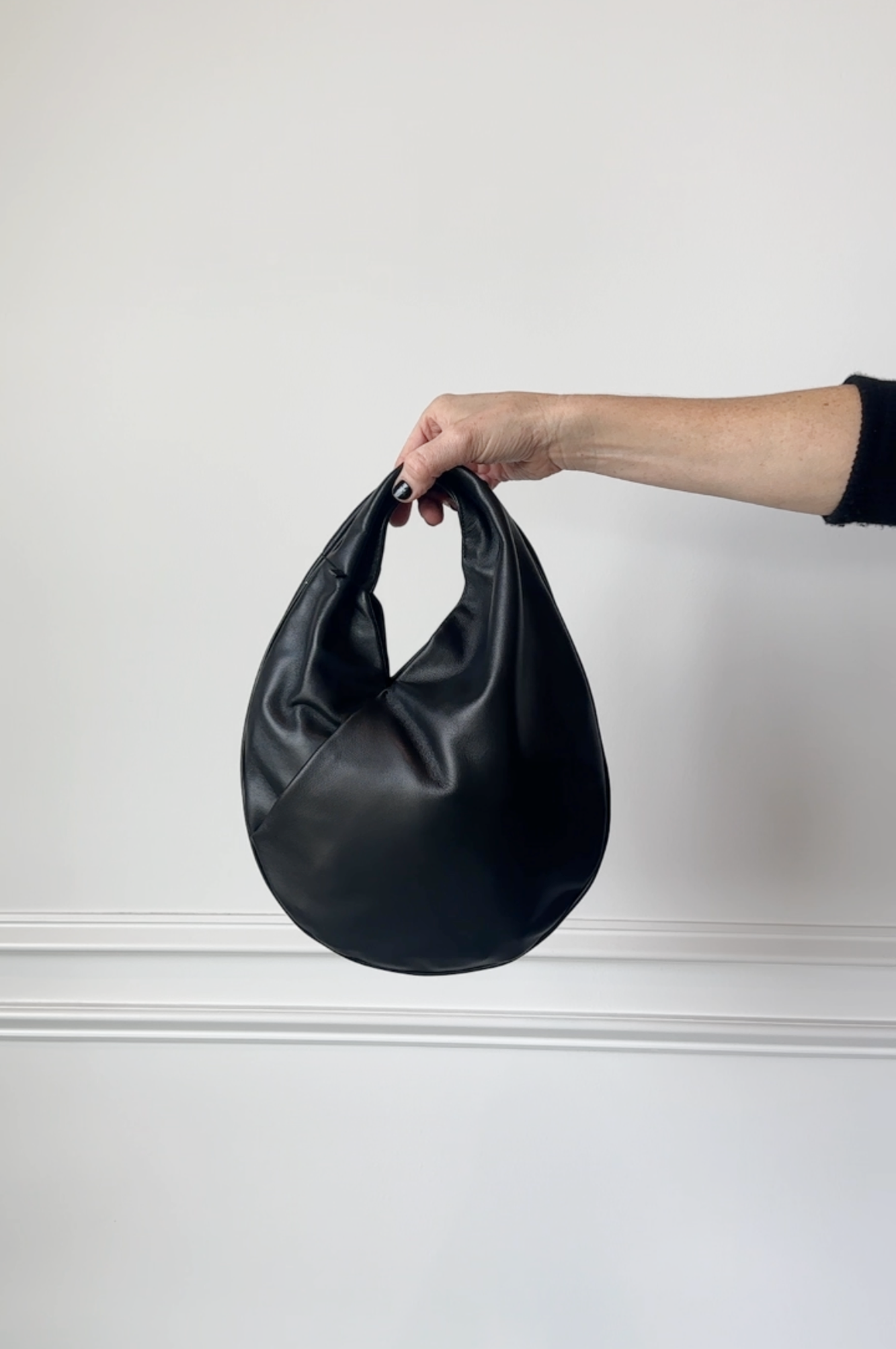 Black leather handbag held by a hand against a white background