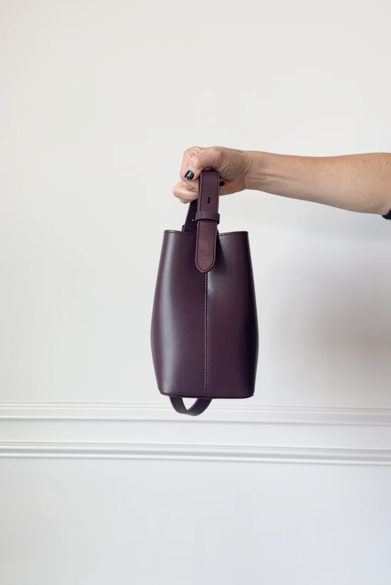 Hand holding a dark purple leather bag against a white background