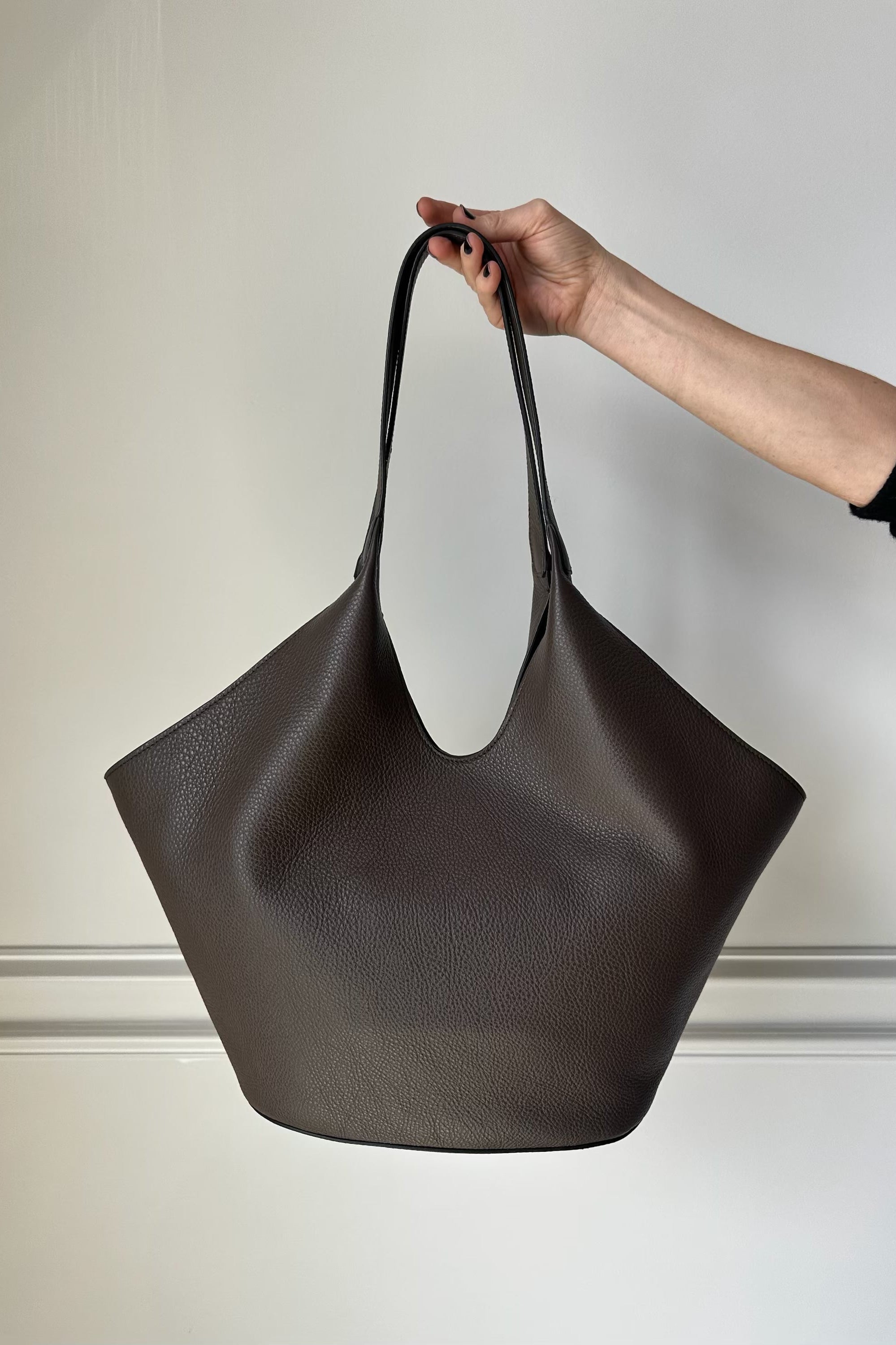 Hand holding a dark brown leather handbag against a neutral background