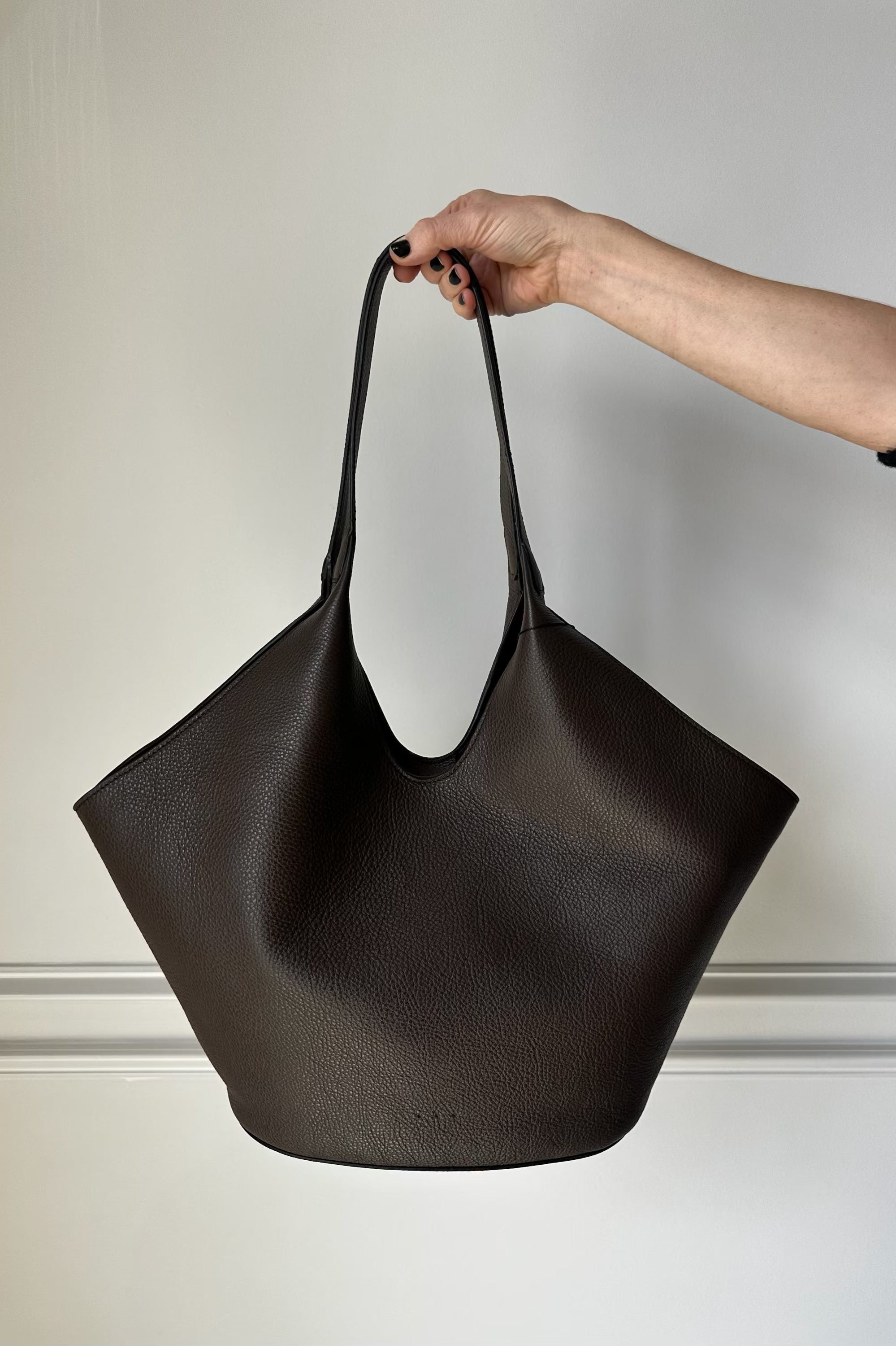 Black handbag held by a person against a neutral background