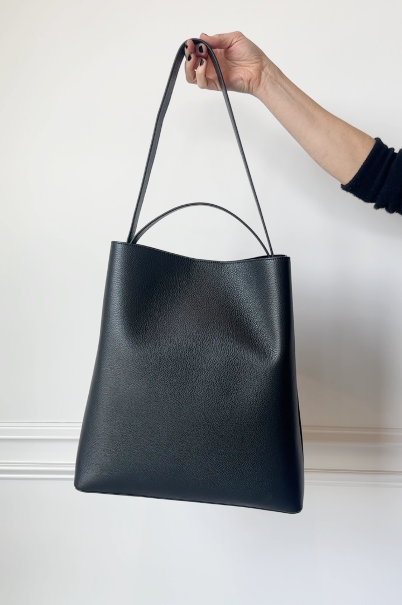 Black leather tote bag held by a hand against a white background