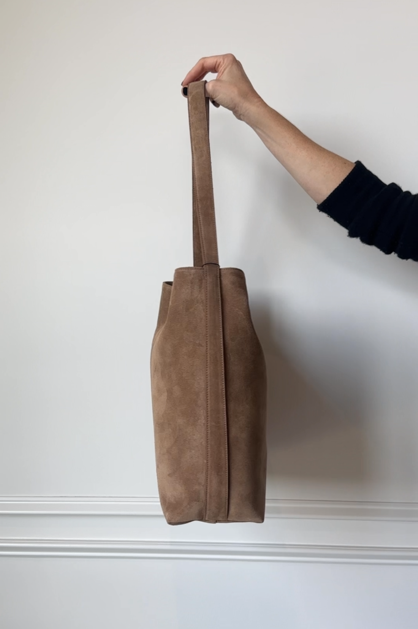 Brown suede handbag held by a person against a white wall