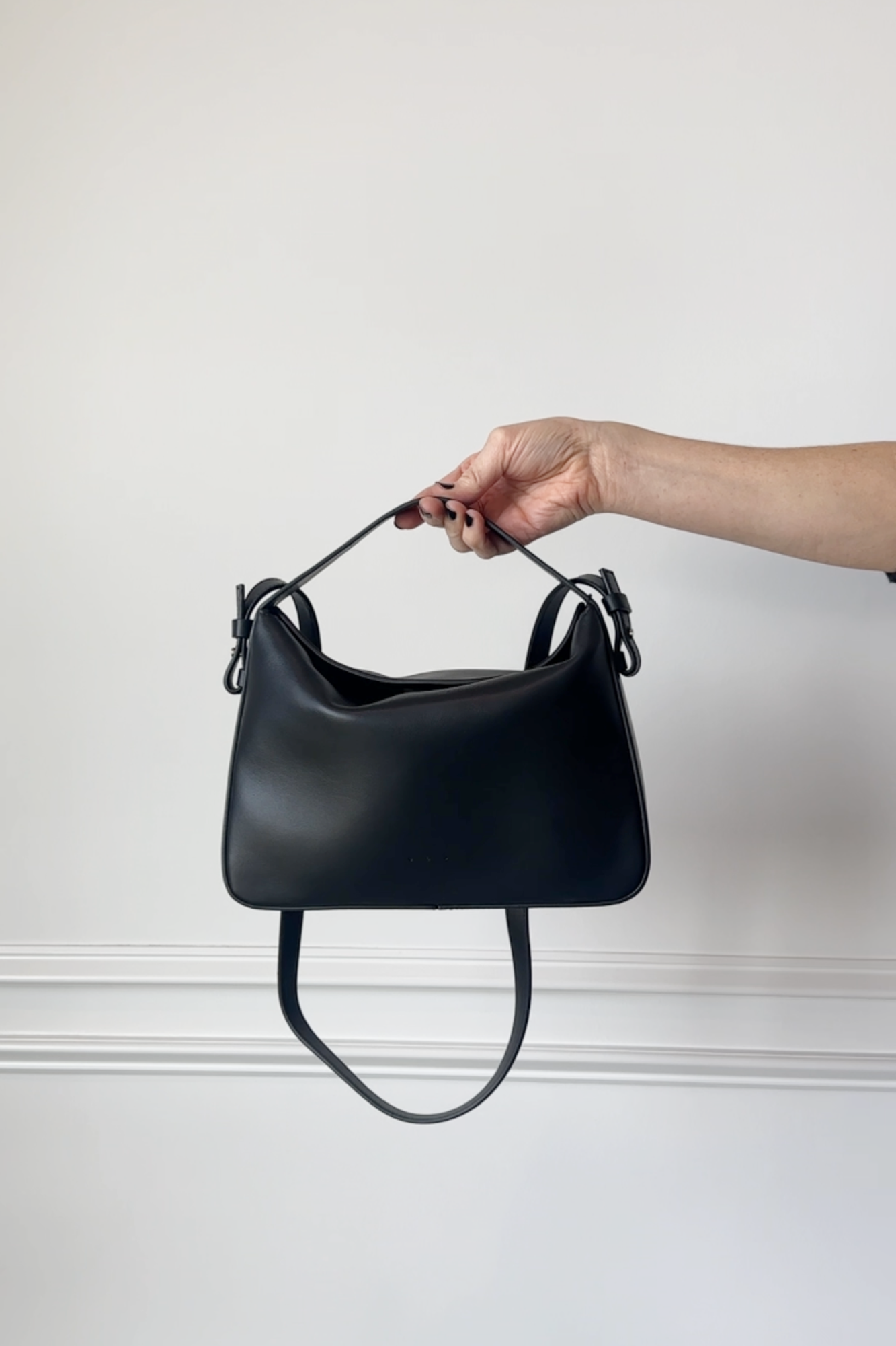 Black handbag held by a hand against a light gray background