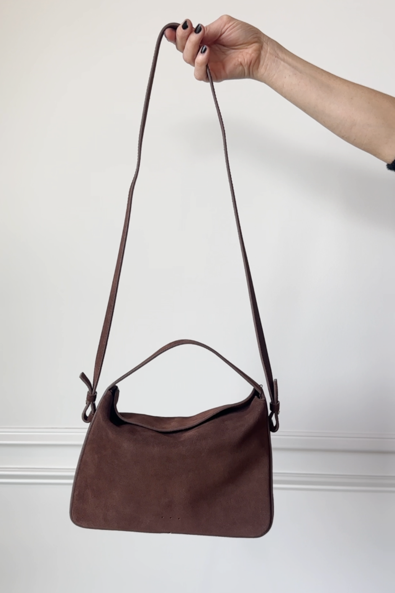 Brown handbag held by a hand against a plain background