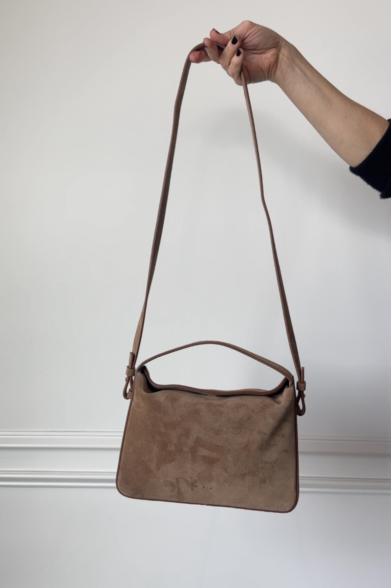 Brown handbag held by a hand against a plain background