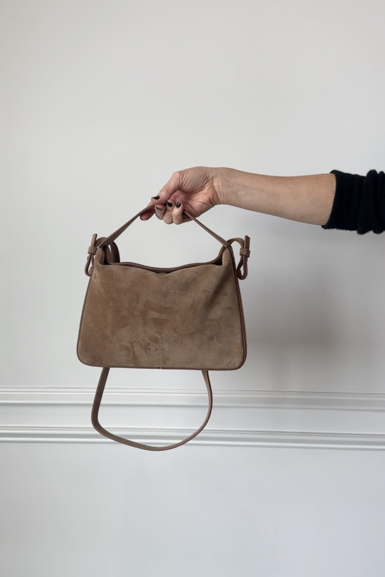 Brown suede handbag held by a hand against a white background