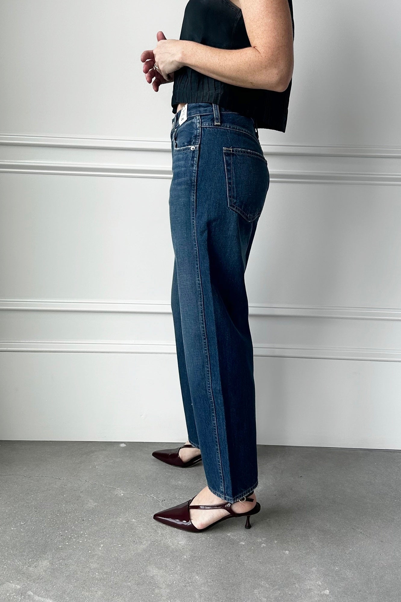 Person wearing blue jeans and a black top against a white wall.
