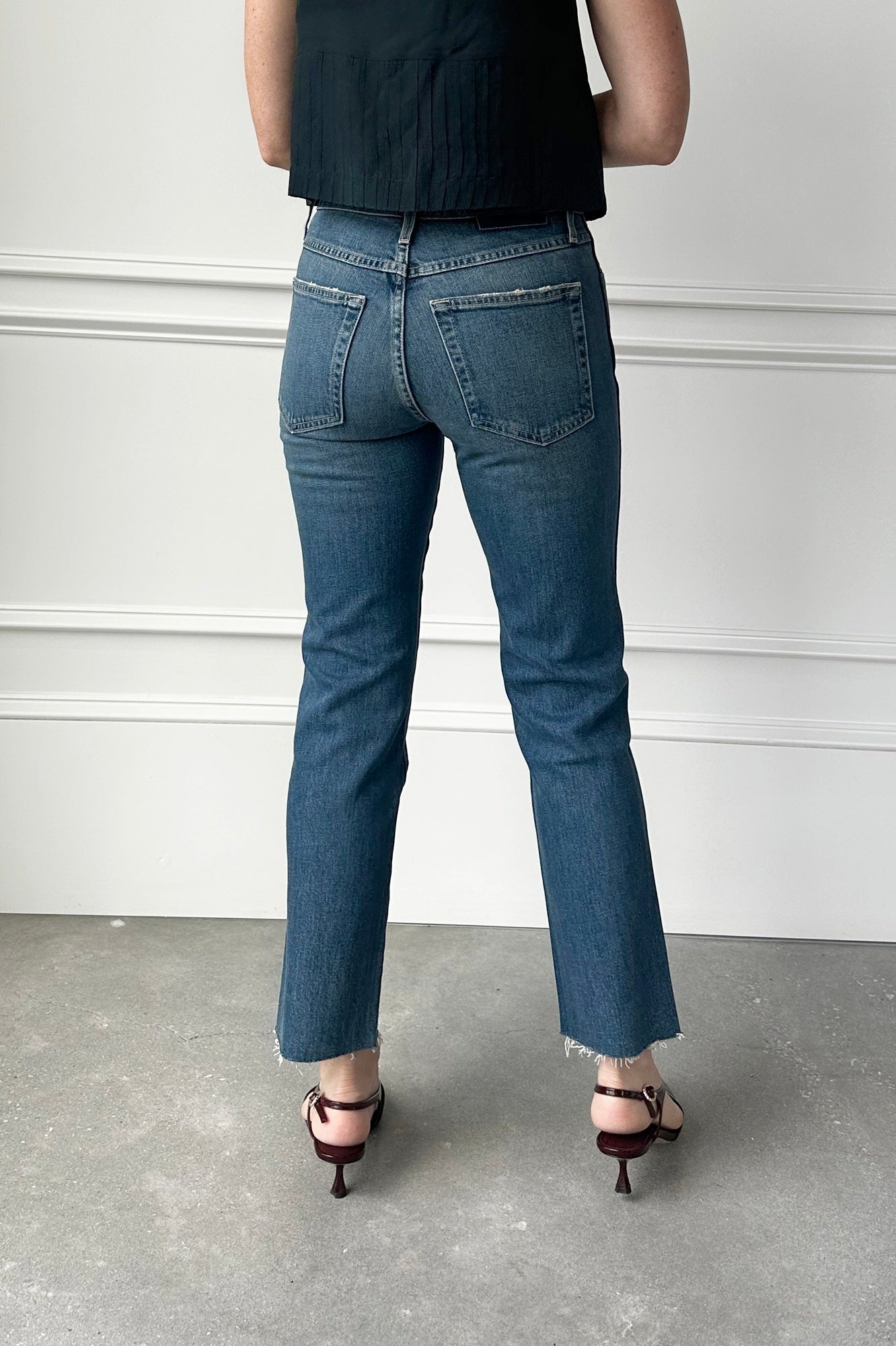 Person wearing blue jeans standing against a white wall.