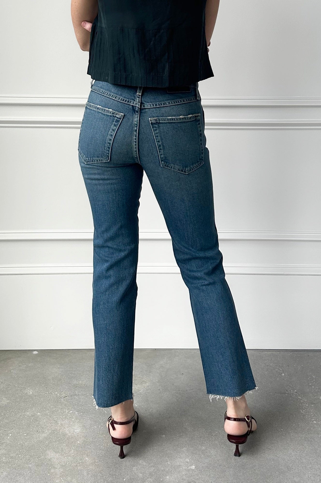 Person wearing blue jeans and black top against a white wall.